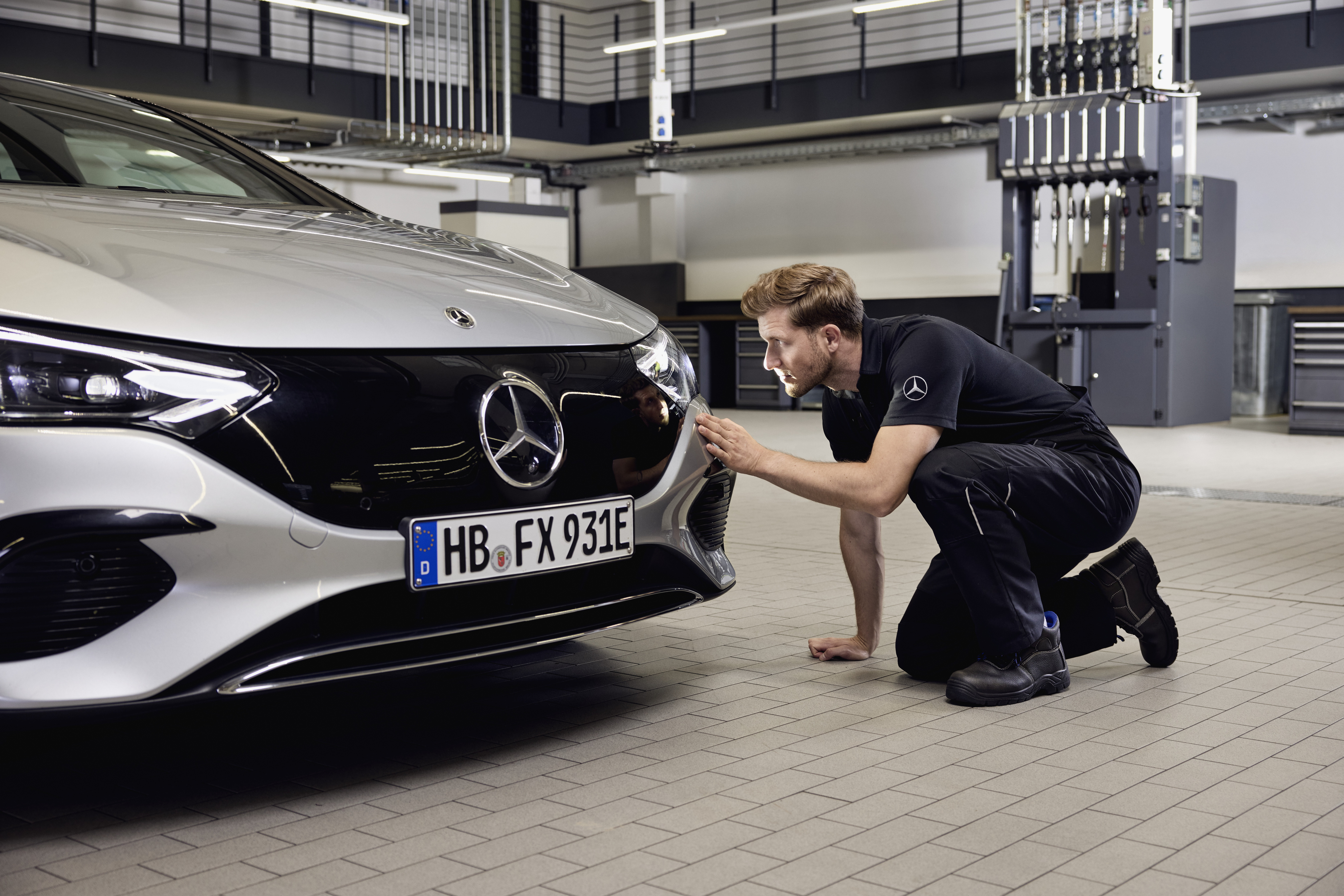 Substituição de faróis originais Mercedes-Benz Grande plano da frente de um veículo Mercedes-Benz com um técnico a examinar pormenorizadamente a substituição de peças originais Mercedes-Benz.