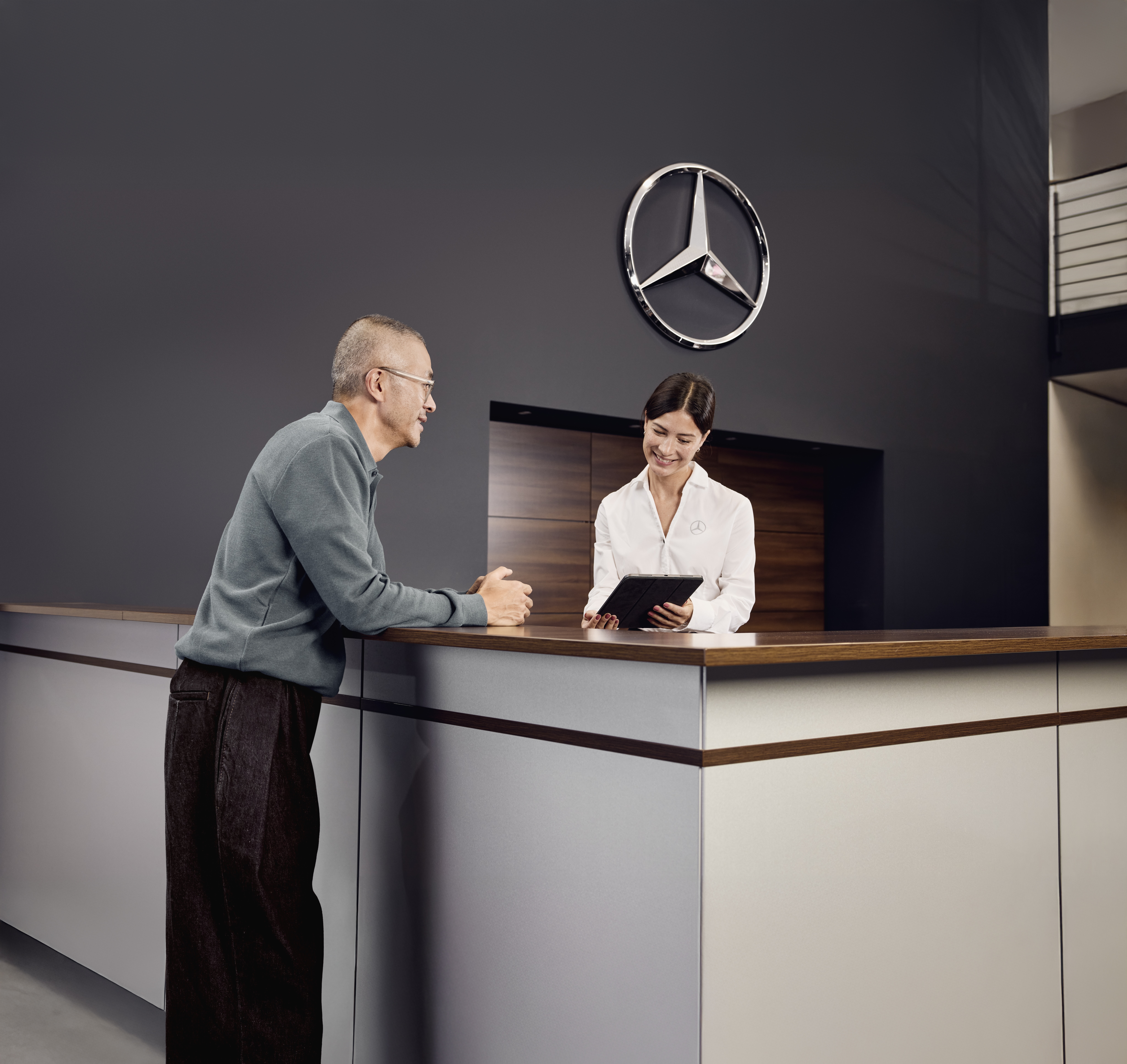 Consulta de Peças Originais Mercedes-Benz Área de receção de serviço num concessionário Mercedes-Benz onde um cliente discute os pormenores do serviço do veículo com um consultor de serviço na receção.