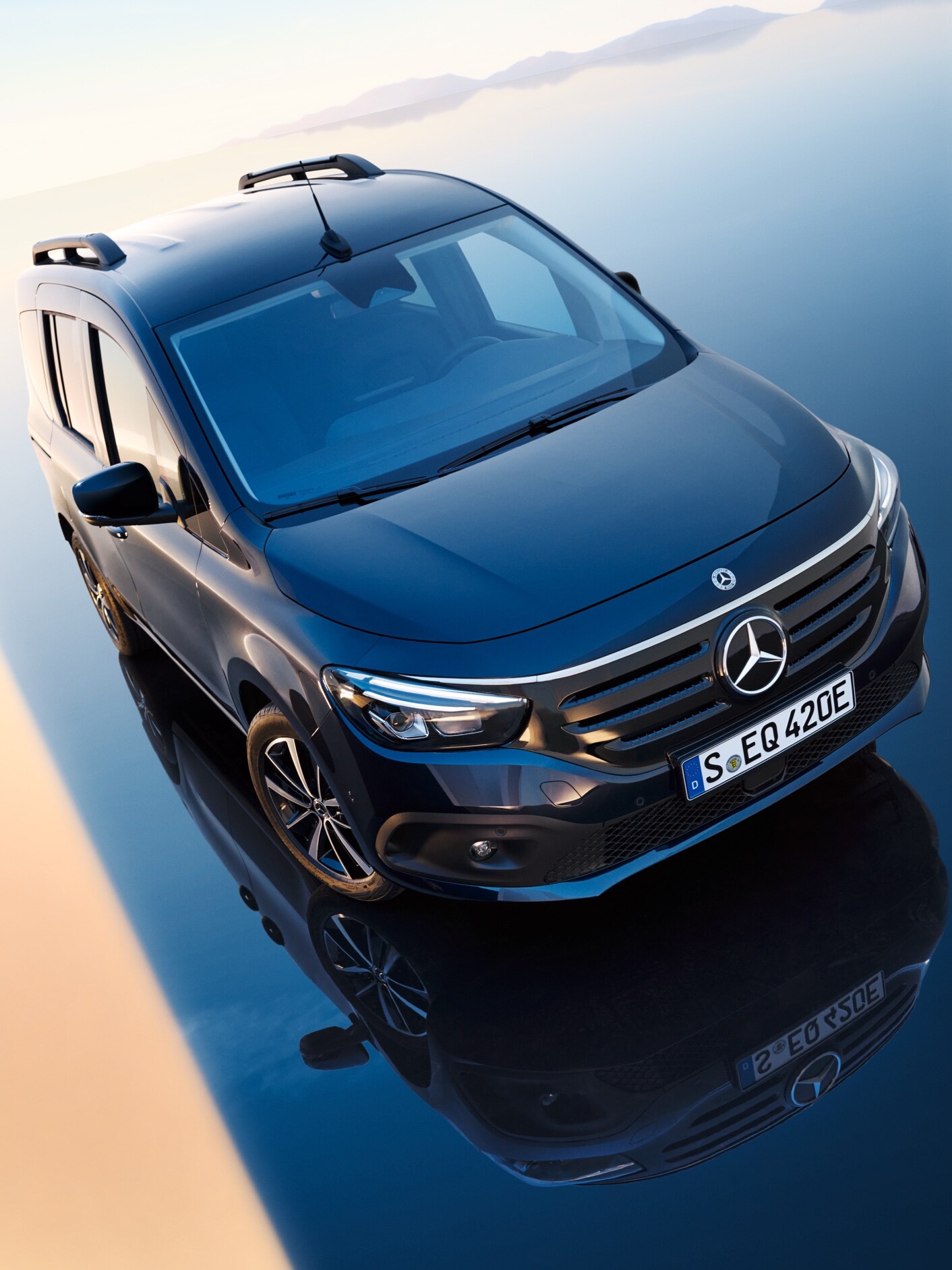O Mercedes-Benz EQT encontra-se sobre uma superfície espelhada que faz lembrar a água - uma cadeia montanhosa pode ser vislumbrada no horizonte.