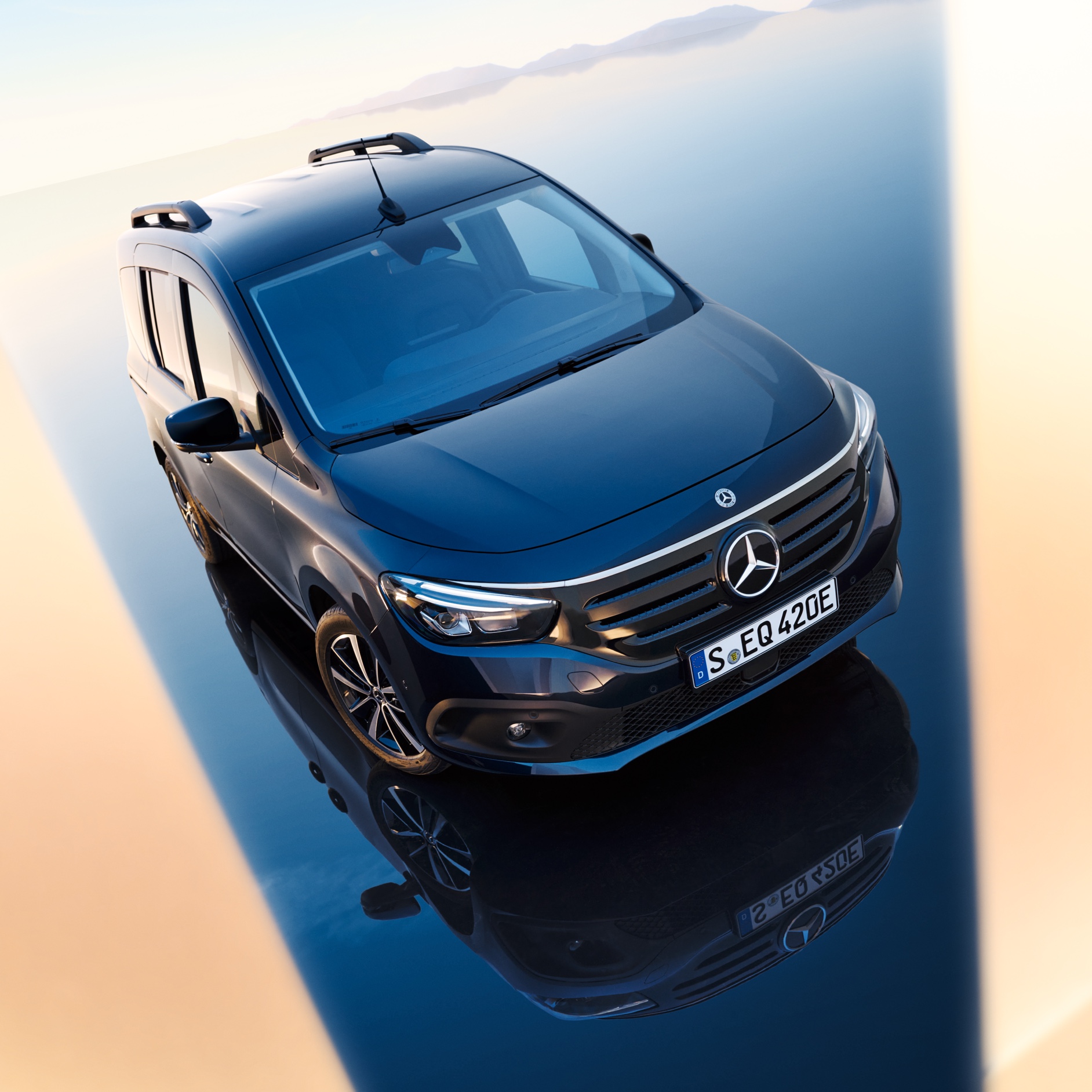 Modelos de furgões e autocaravanas | Mercedes-Benz O Mercedes-Benz EQT encontra-se sobre uma superfície espelhada que faz lembrar a água - uma cadeia montanhosa pode ser vislumbrada no horizonte.