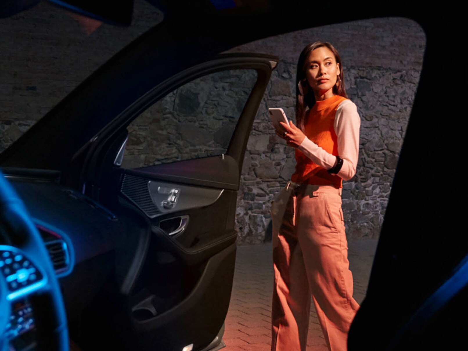 Uma pessoa em frente à porta aberta de um modelo Mercedes-Benz EQ com um smartphone com a aplicação Mercedes me aberta na mão.