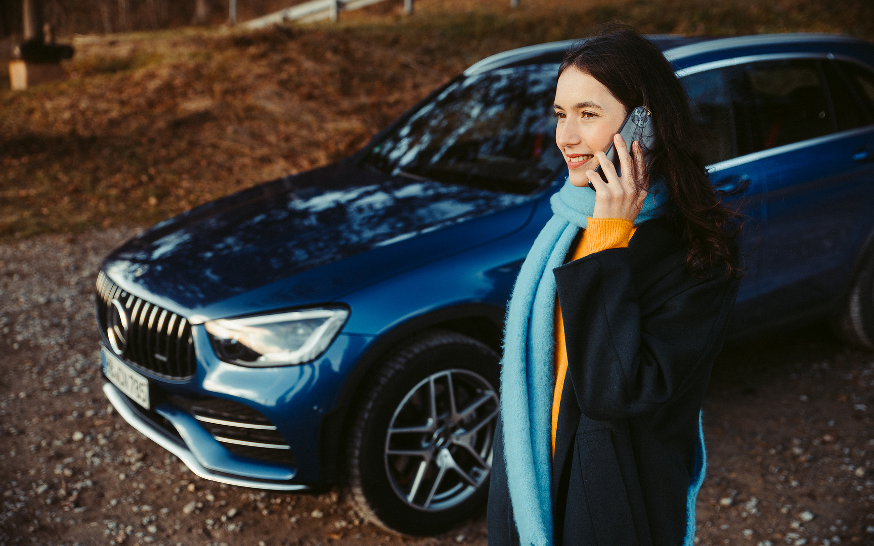 Assistência em viagem | Mercedes-Benz Uma mulher em frente do seu Mercedes SUV a fazer uma chamada com o seu smartphone.