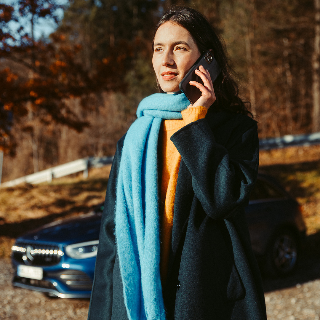 Assistência em viagem | Mercedes-Benz Uma mulher em frente do seu Mercedes SUV a fazer uma chamada com o seu smartphone.