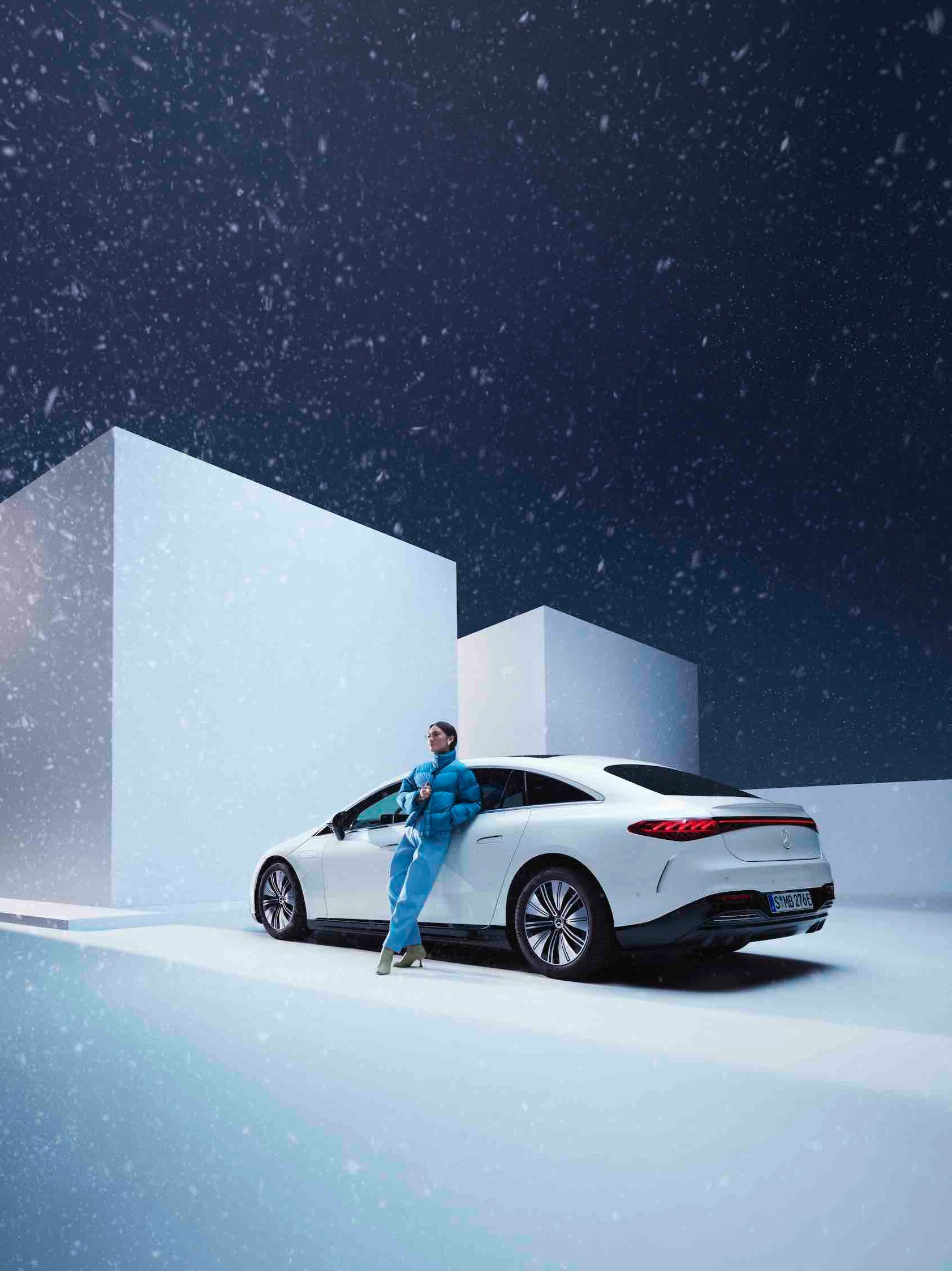 Uma mulher encosta-se ao seu Mercedes enquanto neva.