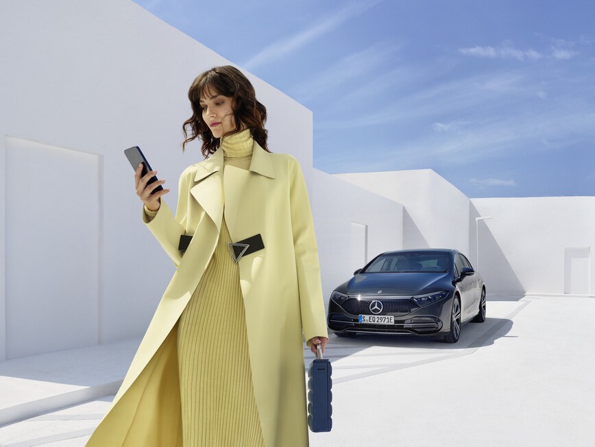 Uma mulher encontra-se com o seu smartphone em frente ao seu Mercedes-Benz.