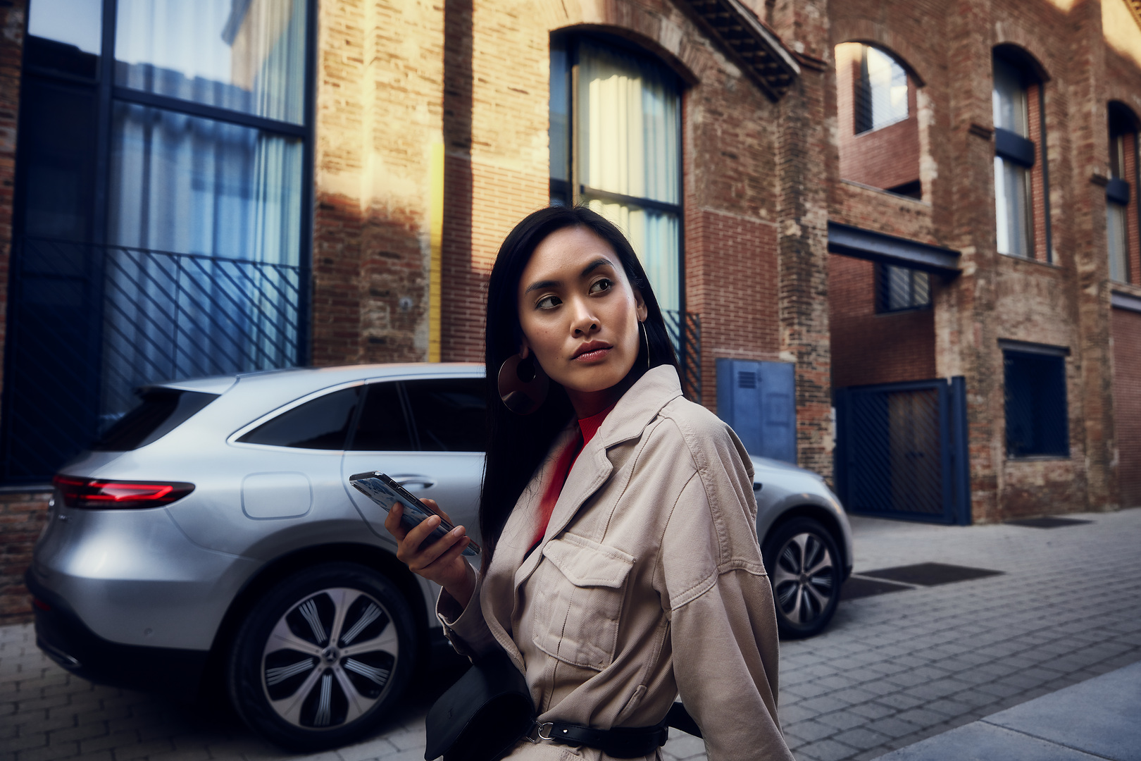 Marcação de data online | Mercedes-Benz Uma mulher em frente ao seu Mercedes com um smartphone na sua mão direita.