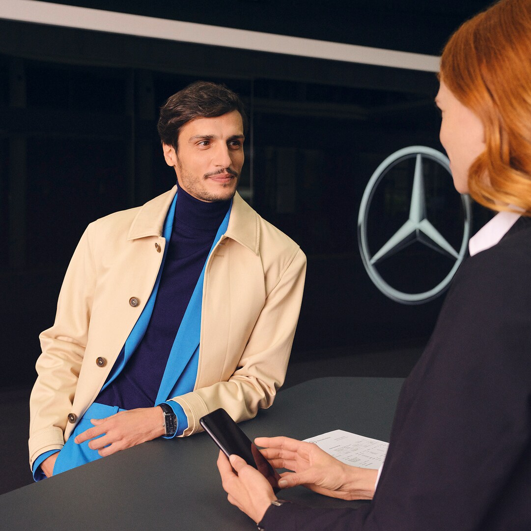 Um cliente debruça-se sobre o balcão e dirige-se com expetativa a um colaborador da Mercedes-Benz.