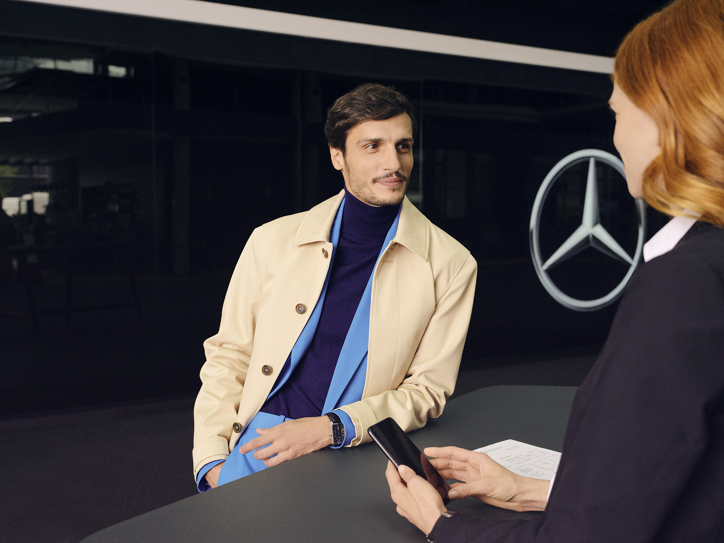 Recolha Mercedes-Benz | Mercedes-Benz Um cliente debruça-se sobre o balcão e dirige-se com expetativa a um colaborador da Mercedes-Benz.