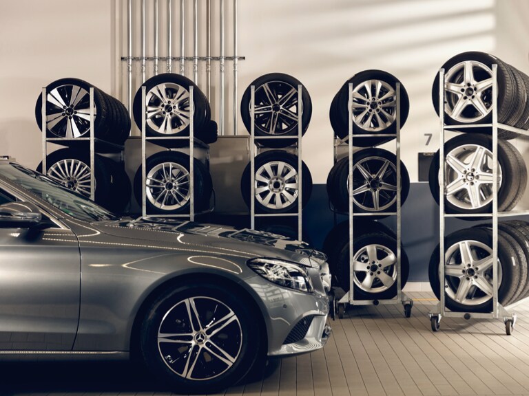 Um Mercedes-Benz em frente a algumas prateleiras com rodas armazenadas.