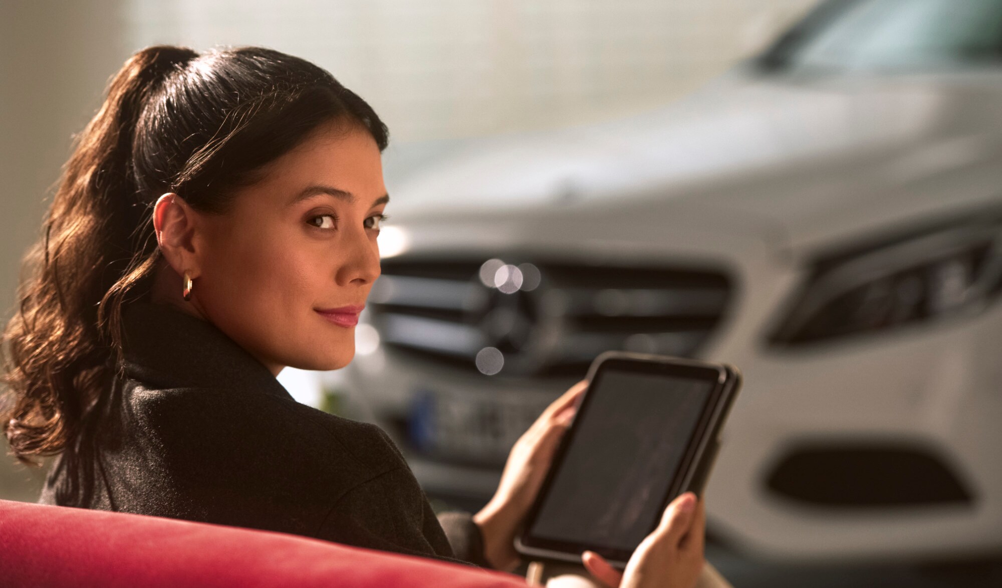 Uma pessoa está sentada ao lado de um veículo Mercedes-Benz com um tablet nas mãos.