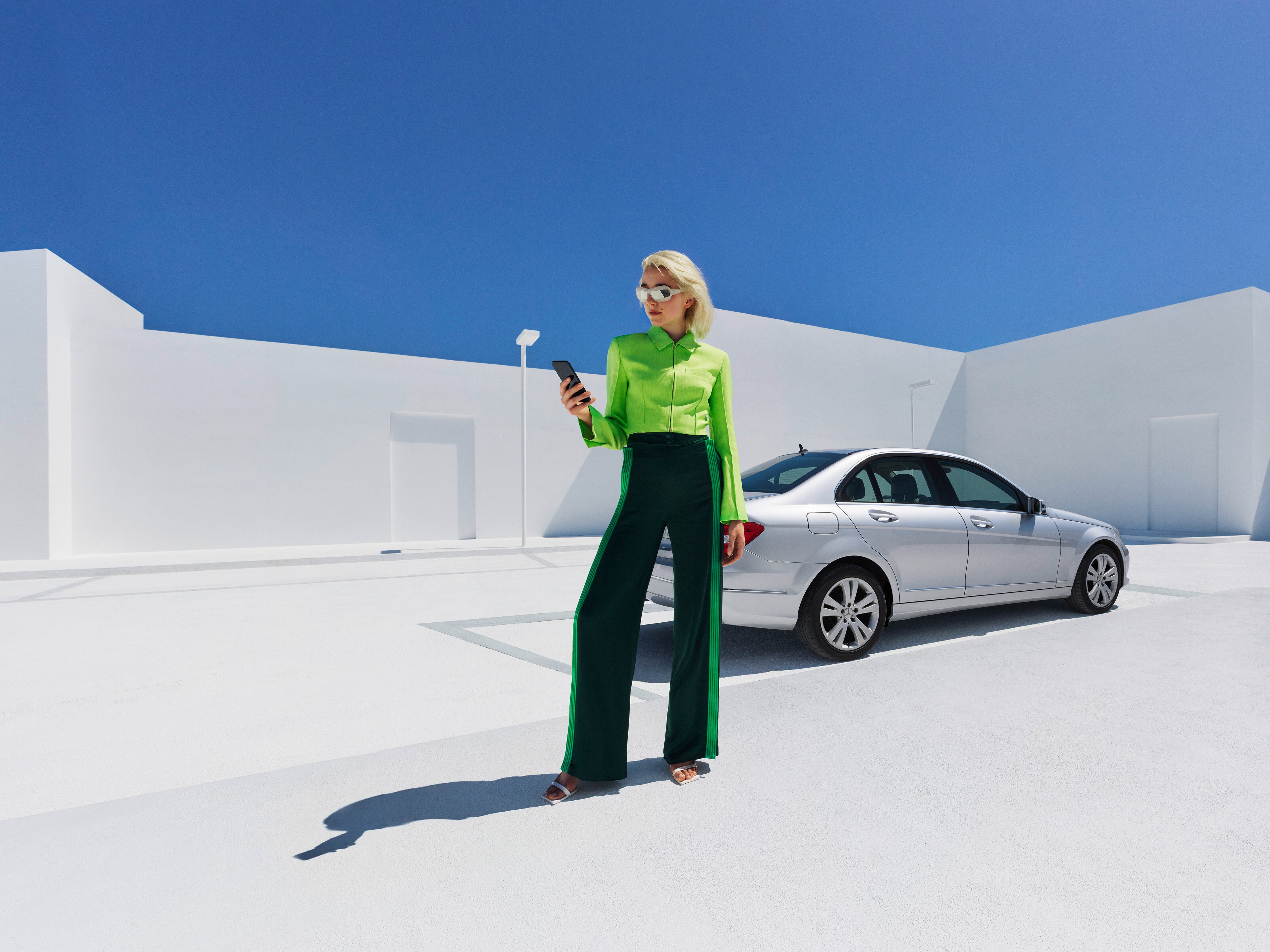 Uma mulher descontraída ao telemóvel em frente ao seu Mercedes.