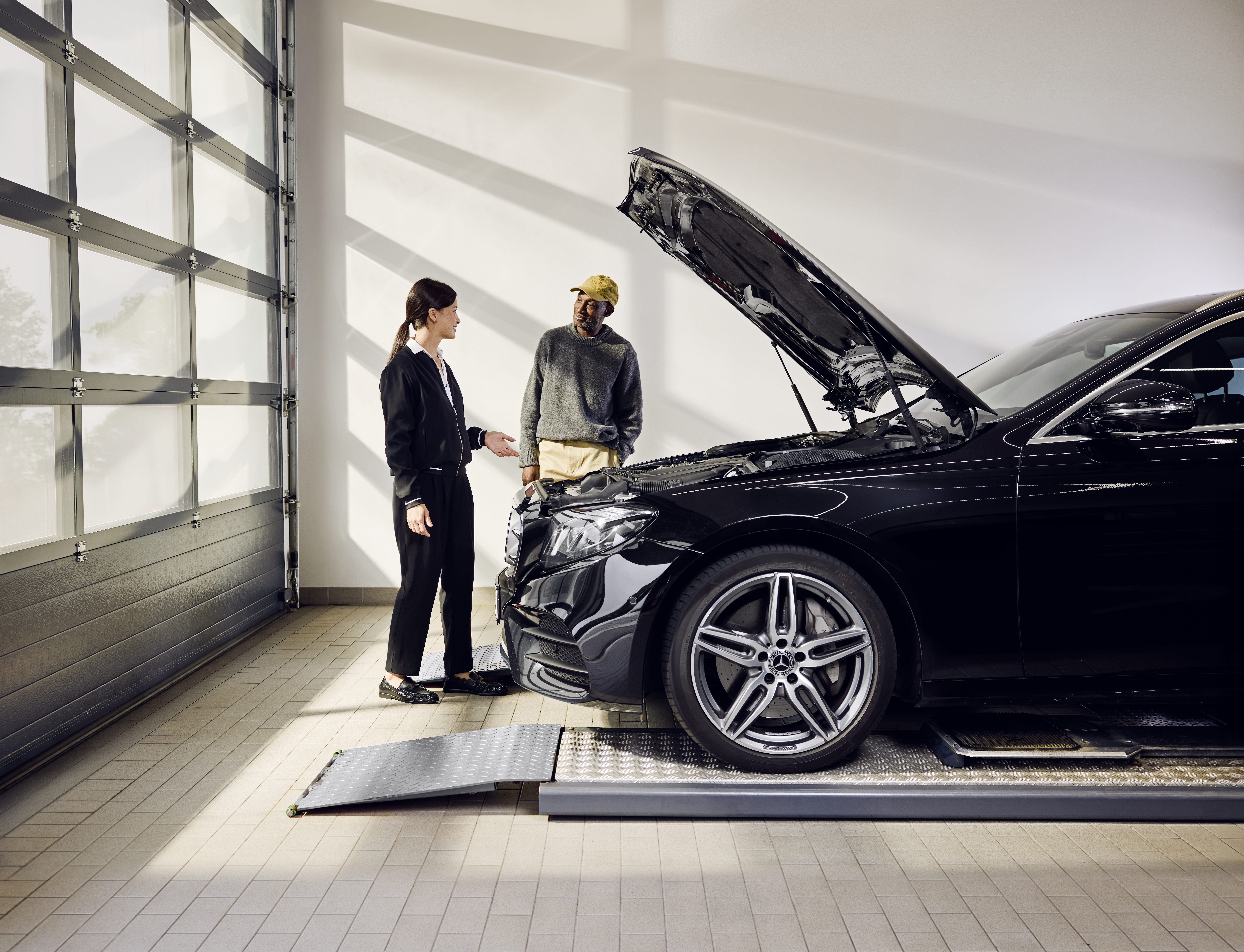 Peças genuínas da Mercedes-Benz Veículo Mercedes-Benz posicionado numa rampa de serviço com o capot aberto durante a substituição profissional de peças originais numa oficina autorizada.