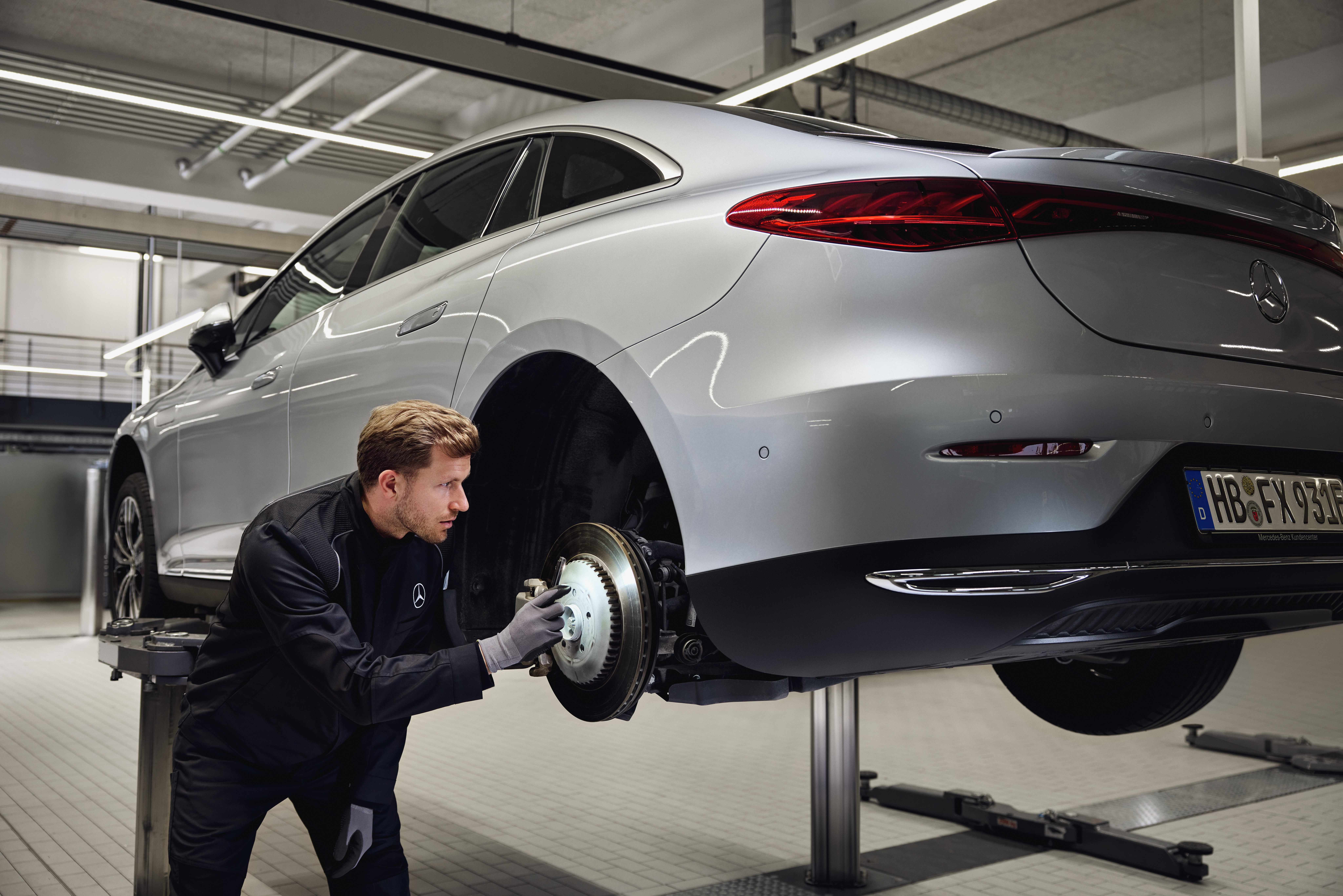 Substituição de travões originais Mercedes-Benz Veículo Mercedes-Benz levantado numa plataforma com um técnico que inspeciona o sistema de travões traseiro para um serviço de substituição de peças originais.