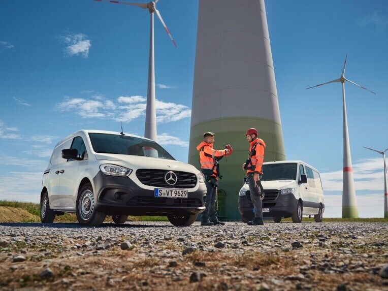 Dois veículos comerciais ligeiros Mercedes-Benz e duas pessoas com vestuário de alta visibilidade em frente a um parque eólico.