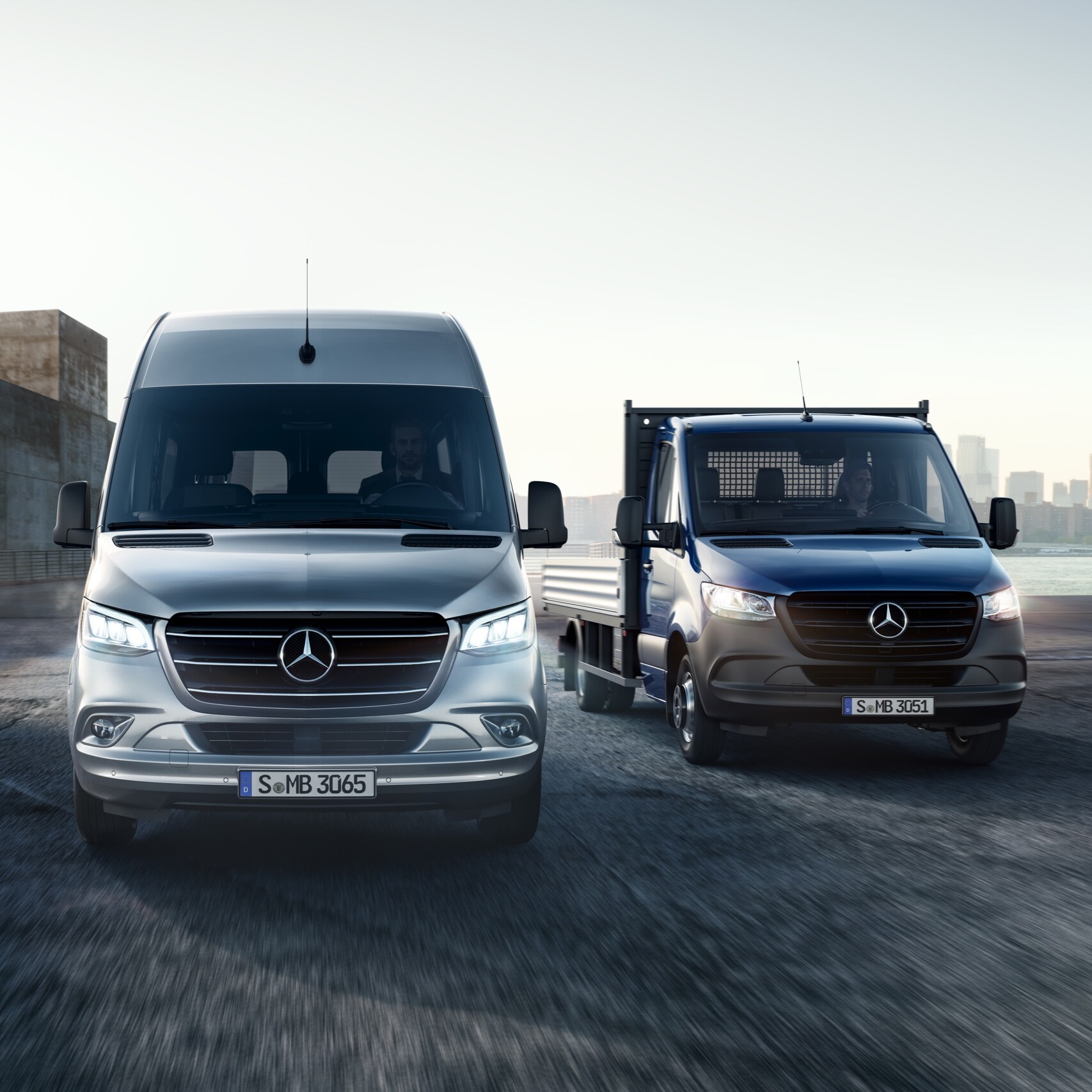 O Mercedes-Benz Sprinter como carroçaria de plataforma e furgão lado a lado em frente a um conjunto de edifícios modernos.