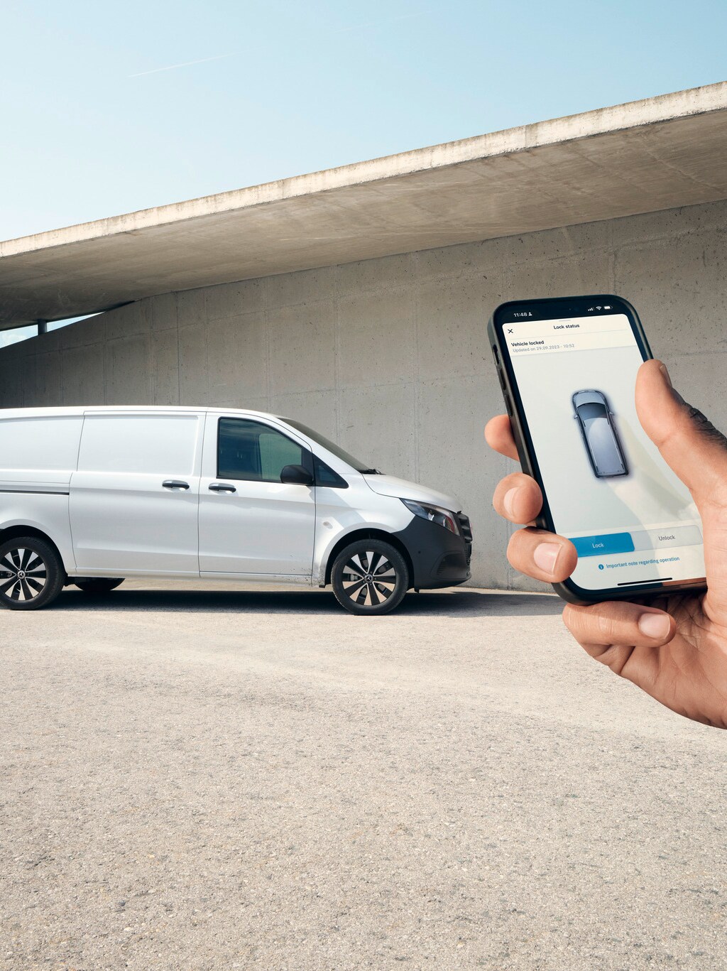 Uma mão a segurar um smartphone que apresenta a aplicação Mercedes me. O Vito Furgão em segundo plano.