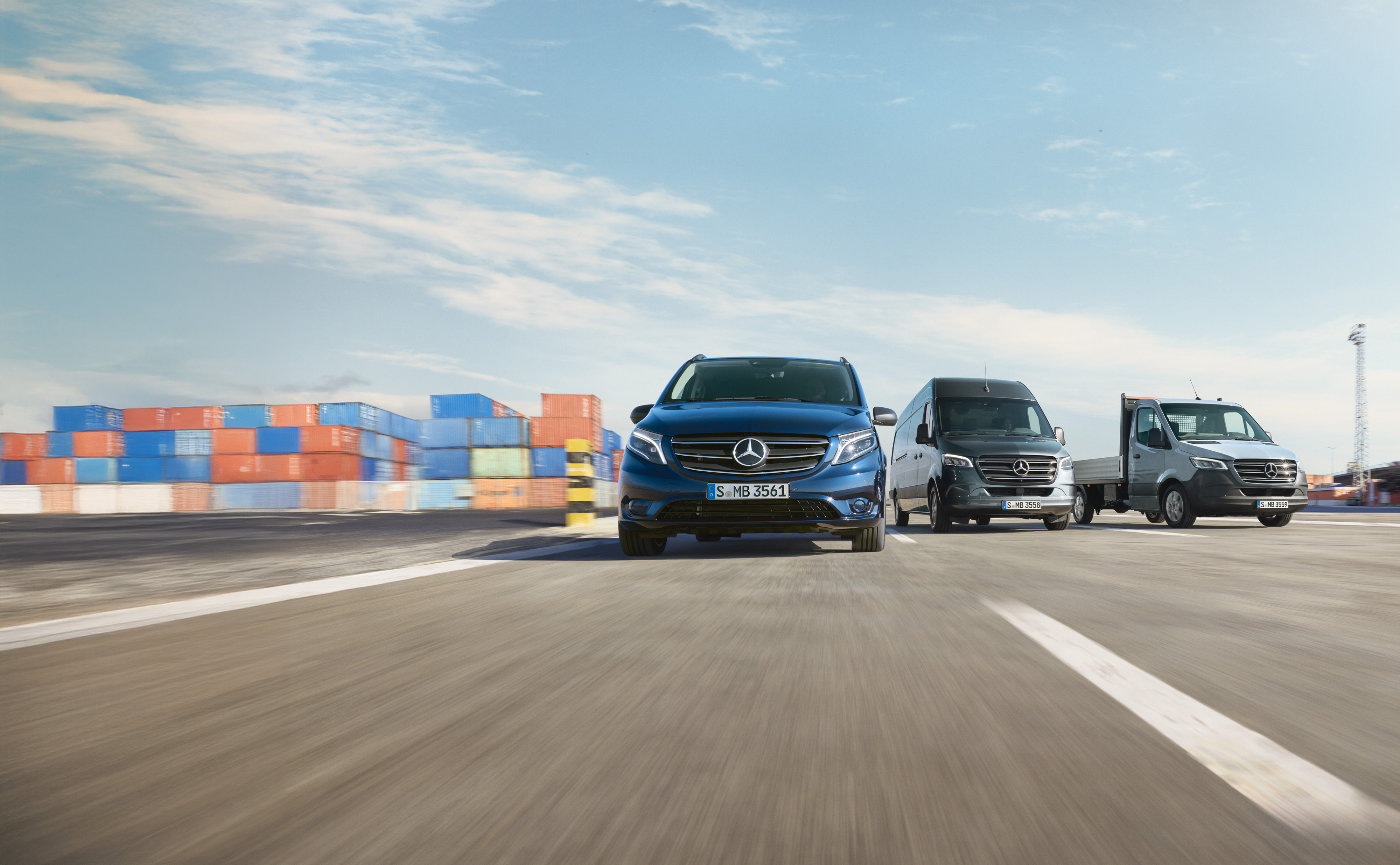 Mercedes-Benz | Assistência de veículos comerciais ligeiros | Service24h Uma série de veículos comerciais ligeiros Mercedes-Benz estacionados lado a lado numa estrada junto a um cais de expedição.