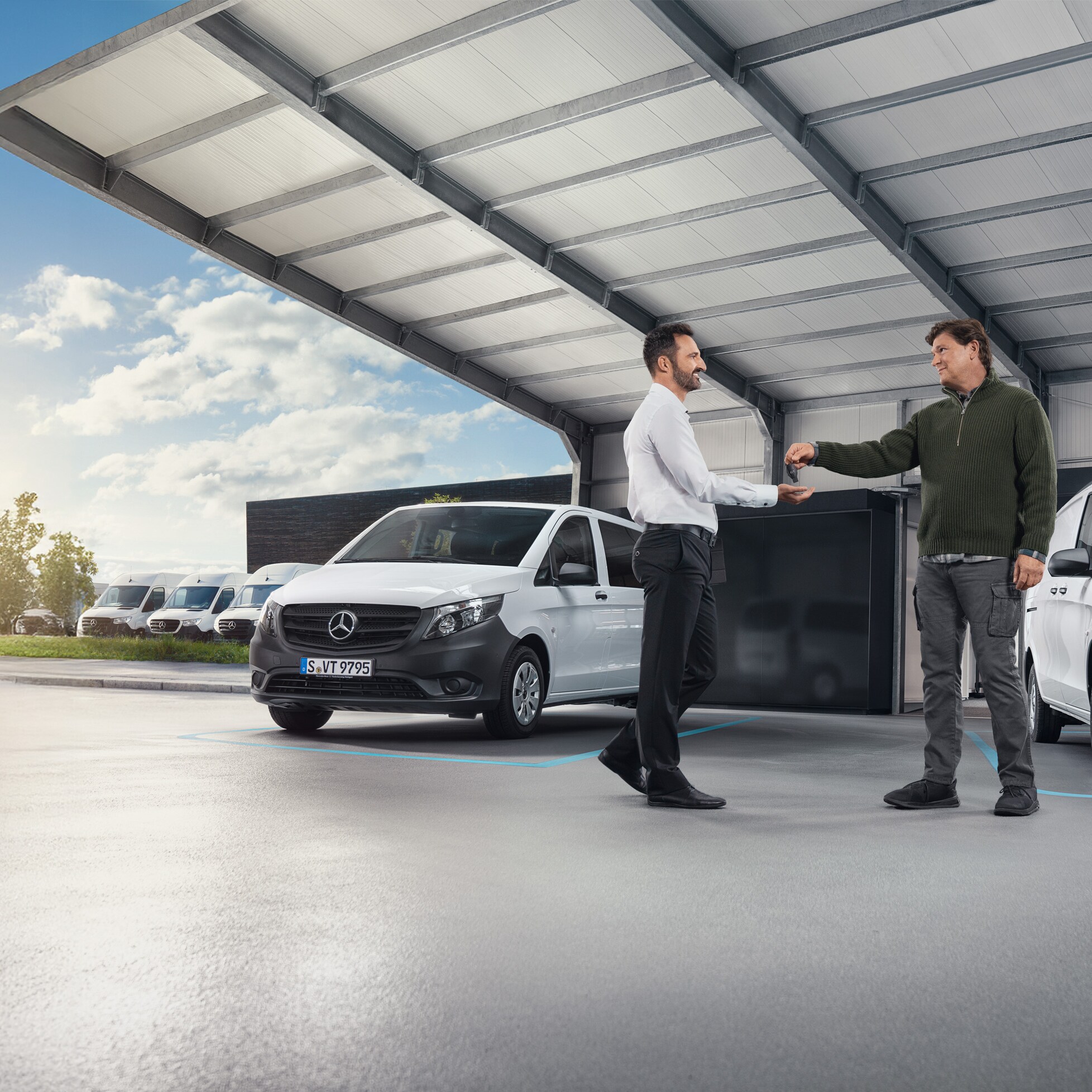 Two men discussing in front of a range of white Mercedes-Benz vans in a hall 