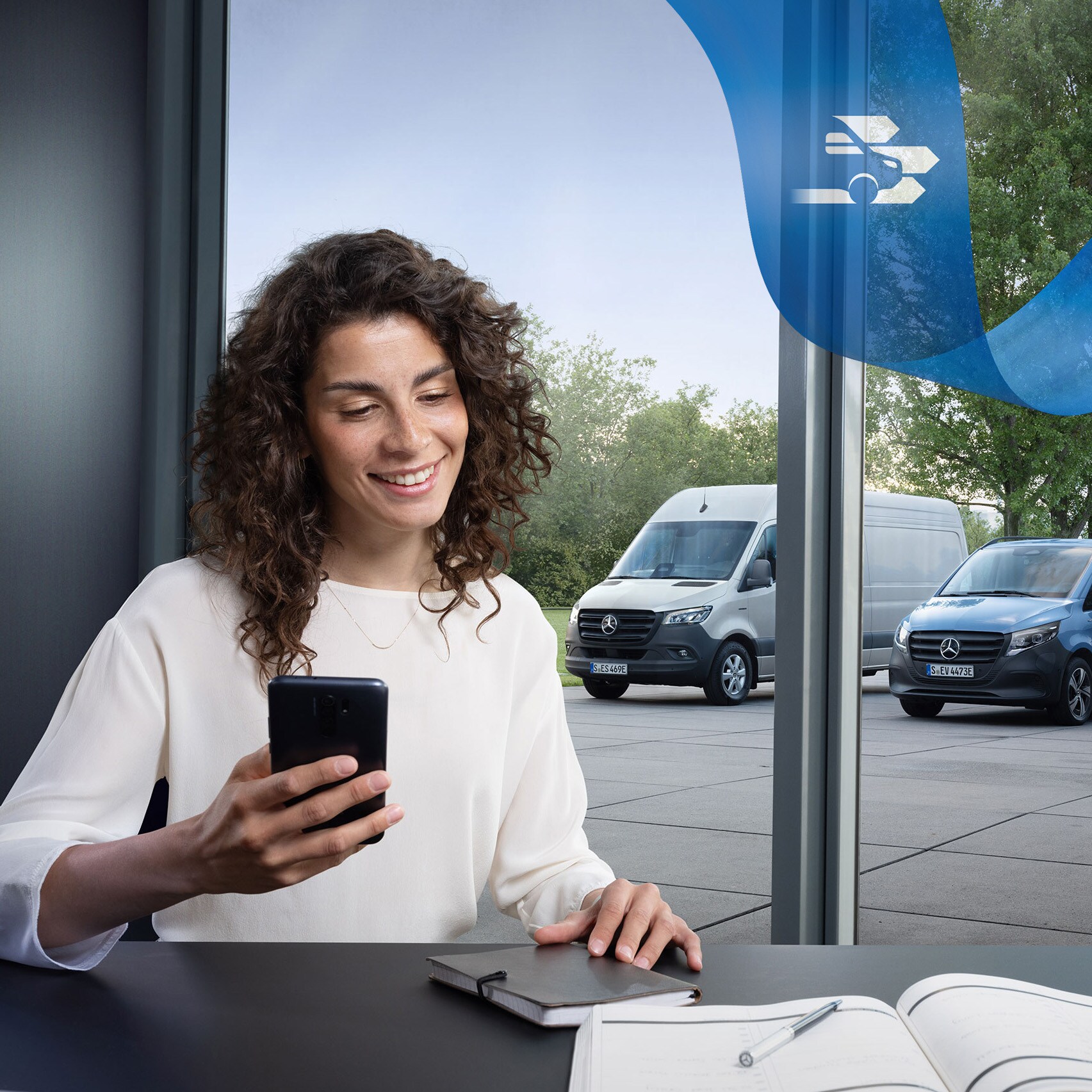 Mulher sentada à secretária com um smartphone e uma série de veículos comerciais ligeiros Mercedes-Benz em segundo plano.