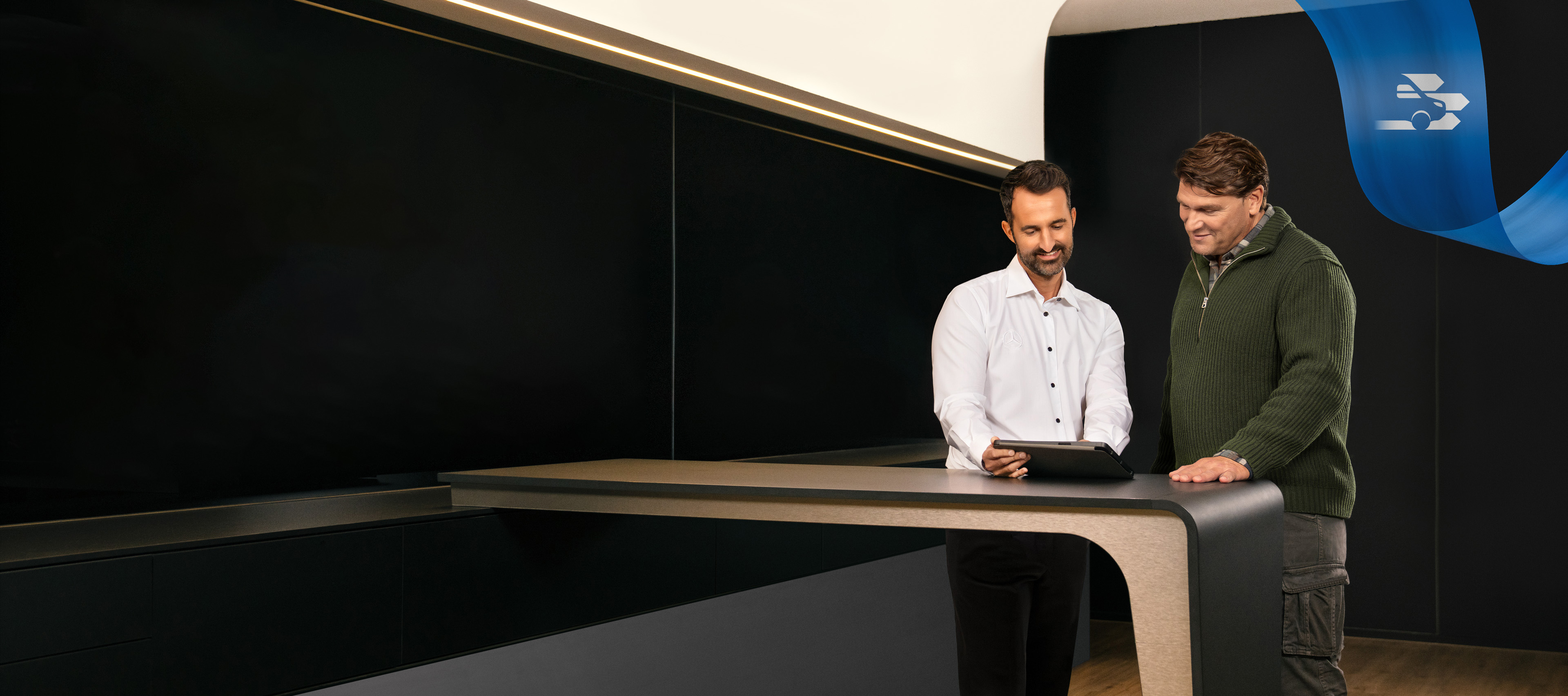 Mercedes-Benz | Conforto | Oficina Autorizada Dois homens de pé num escritório de uma Oficina Autorizada Mercedes-Benz, a falar sobre algo visto num tablet