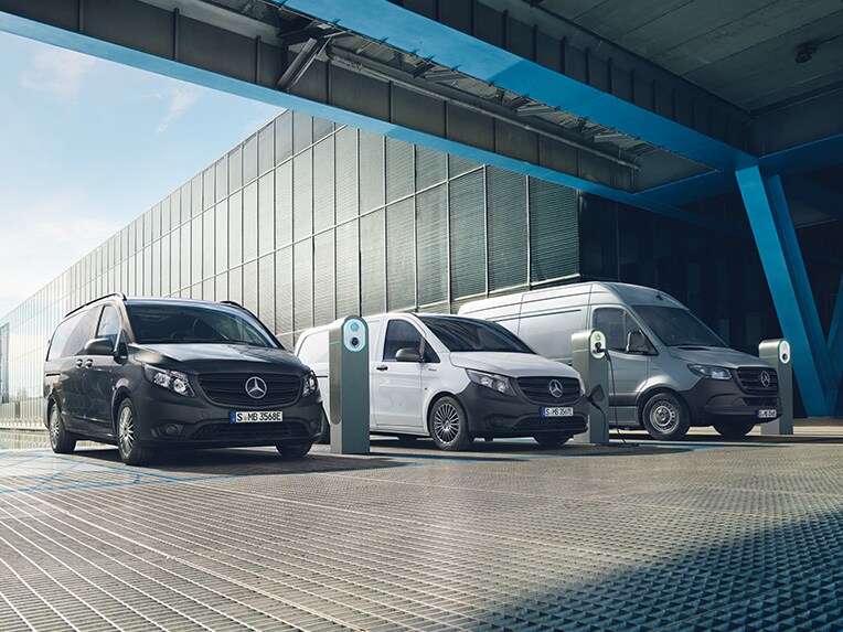 A imagem mostra três veículos comerciais ligeiros elétricos Mercedes-Benz ligados a estações de carregamento.