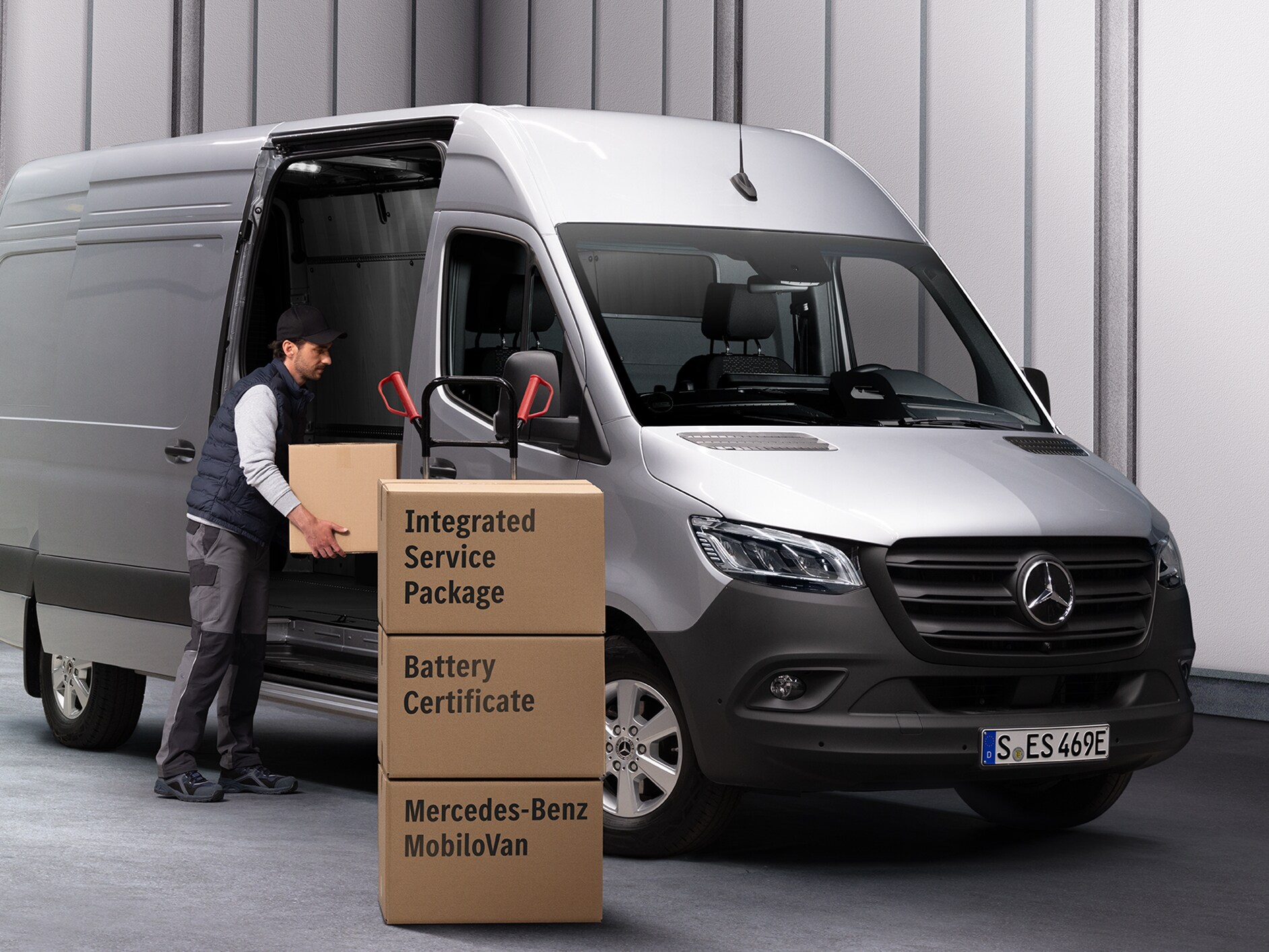 Uma pessoa descarrega caixas de um Mercedes-Benz eSprinter. Três caixas estão empilhadas em frente ao furgão. As caixas estão identificadas com nomes de produtos do Mercedes-Benz Service.