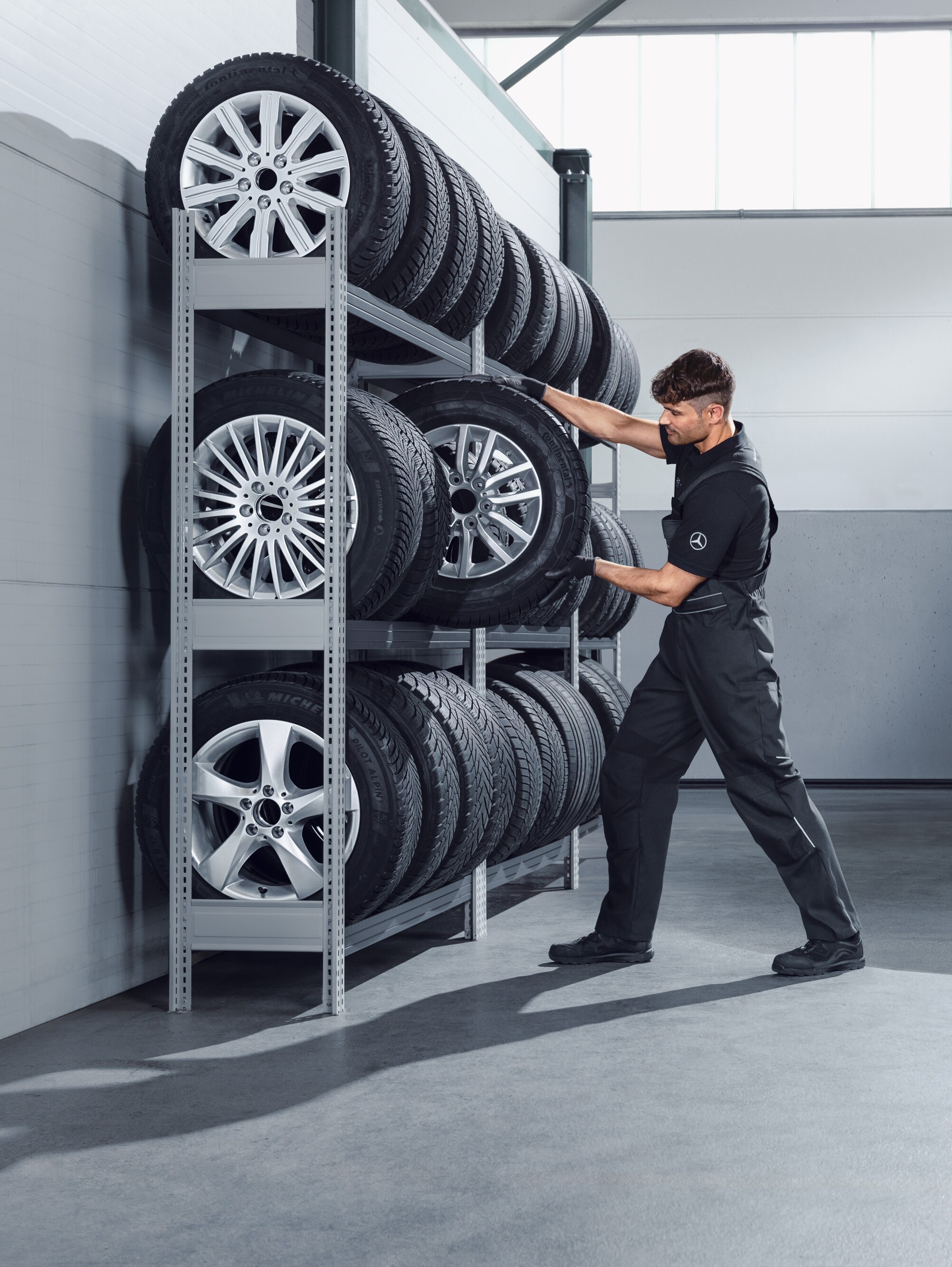 Mecânico a selecionar rodas de inverno completas da Mercedes-Benz para um Sprinter branco, na prateleira da oficina.