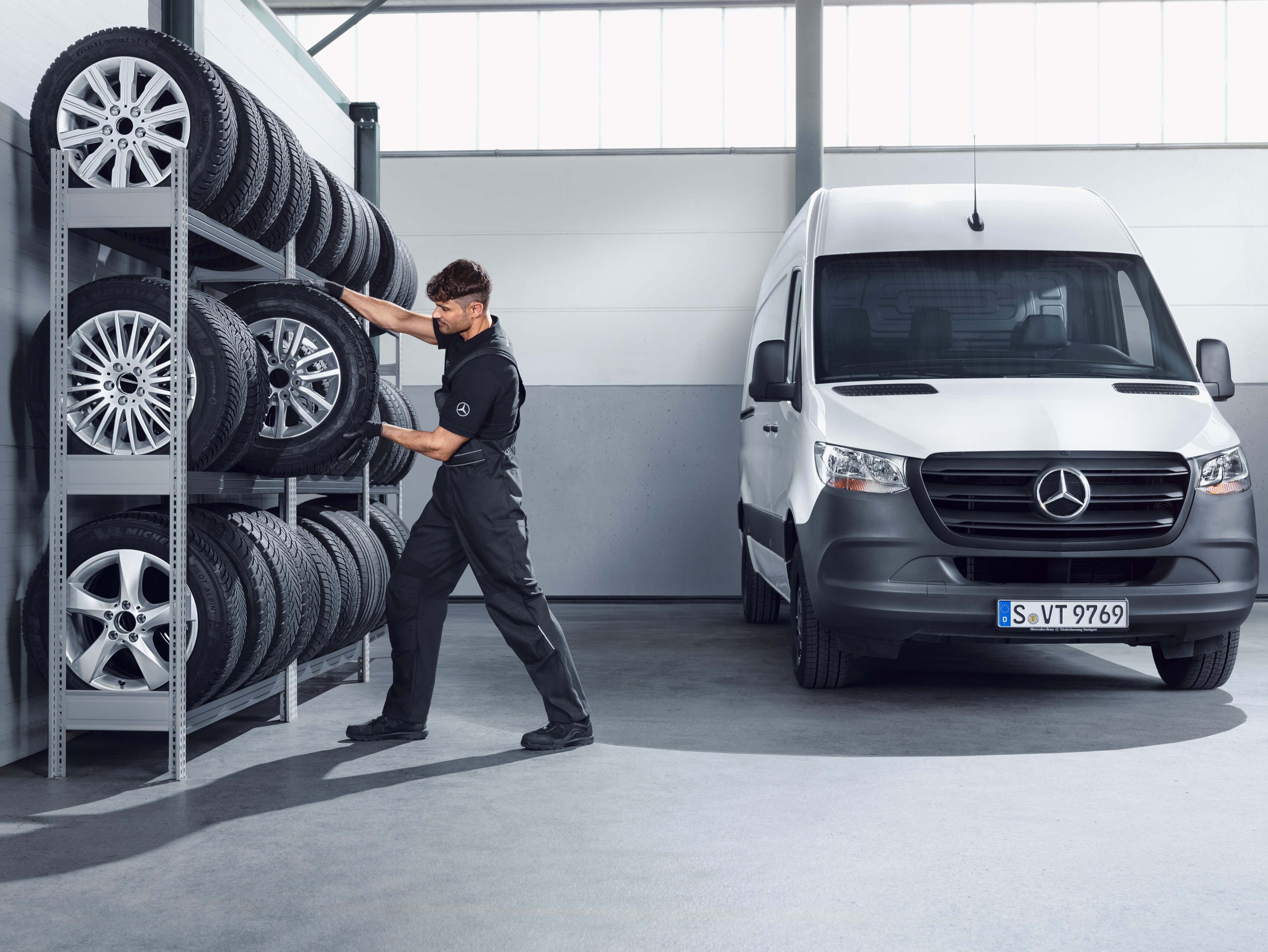 Mecânico a selecionar rodas de inverno completas da Mercedes-Benz para um Sprinter branco, na prateleira da oficina.