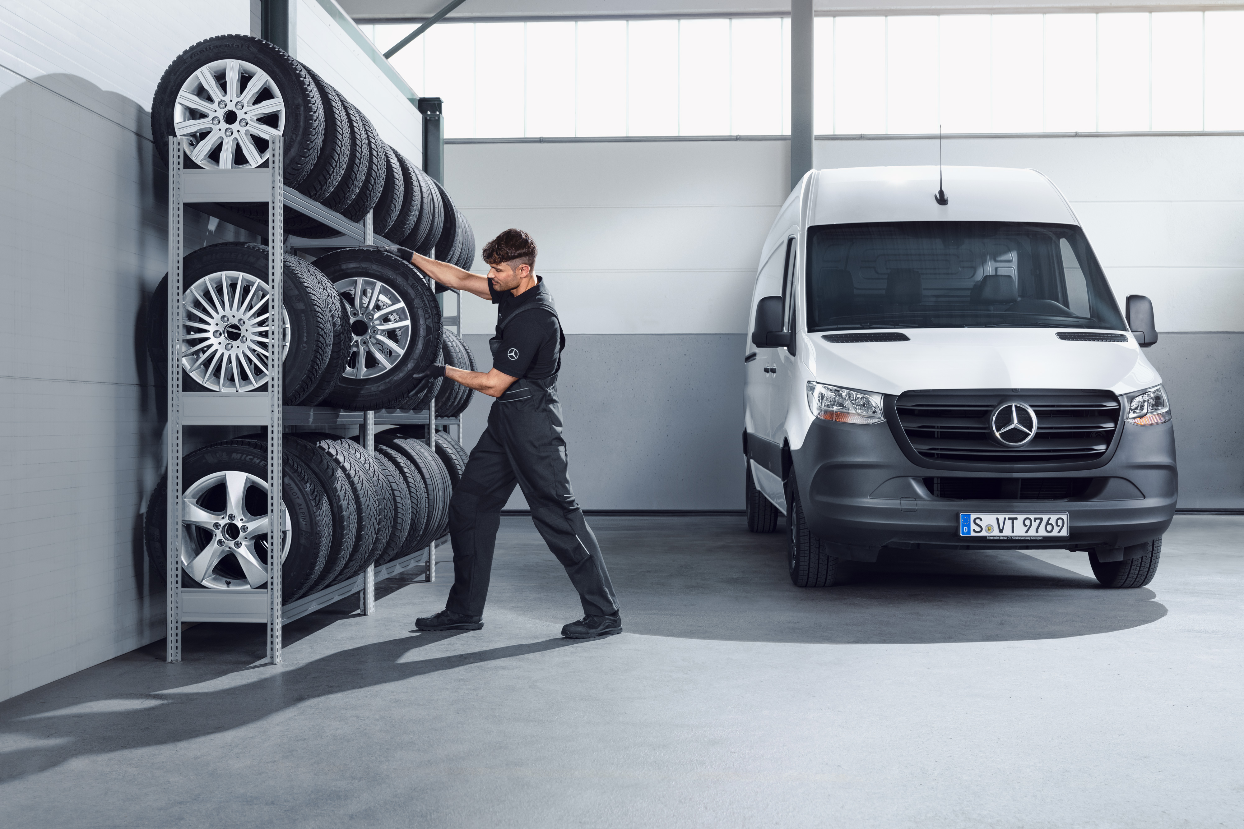 Mercedes-Benz | Carrinhas Peças Genuínas de Qualidade Mecânico a selecionar rodas de inverno completas da Mercedes-Benz para um Sprinter branco, na prateleira da oficina.