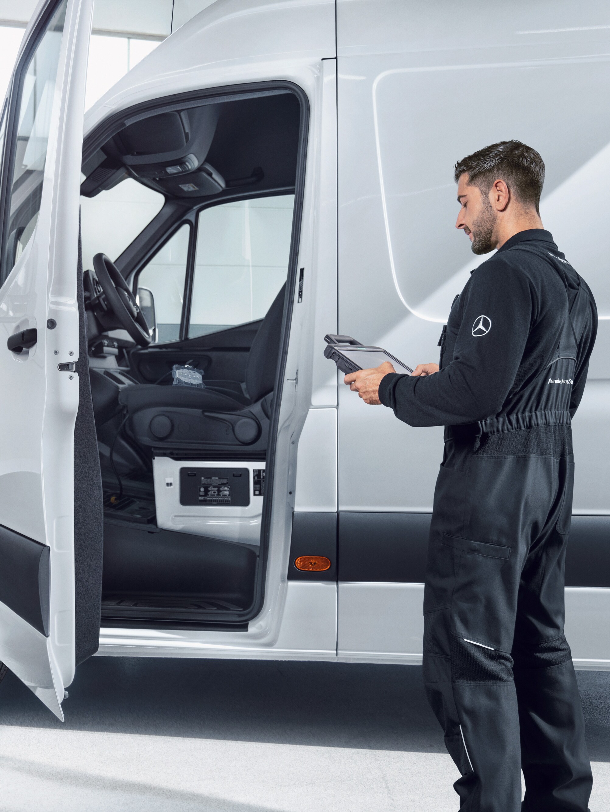 Mecânico a verificar um veículo comercial ligeiro Mercedes-Benz branco com um tablet, simbolizando as normas de qualidade e a promessa de qualidade.