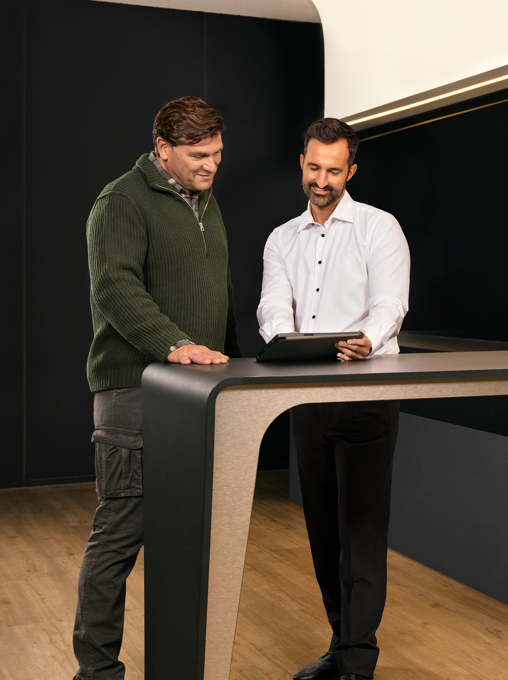 Dois homens numa consulta, de pé à volta de uma mesa, a olhar para um iPad.