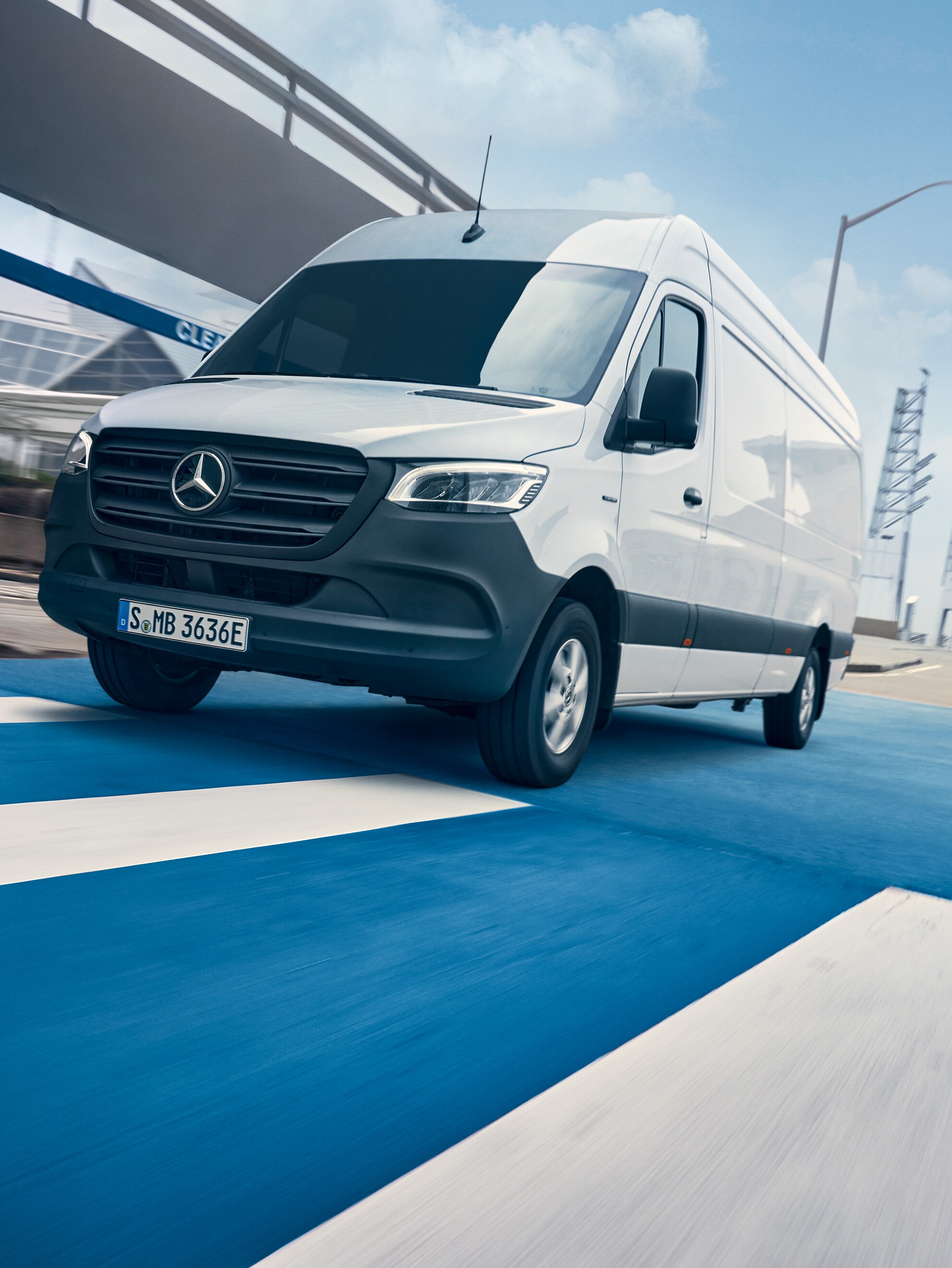 Um Mercedes-Benz Sprinter branco circula numa estrada que atravessa uma cidade.