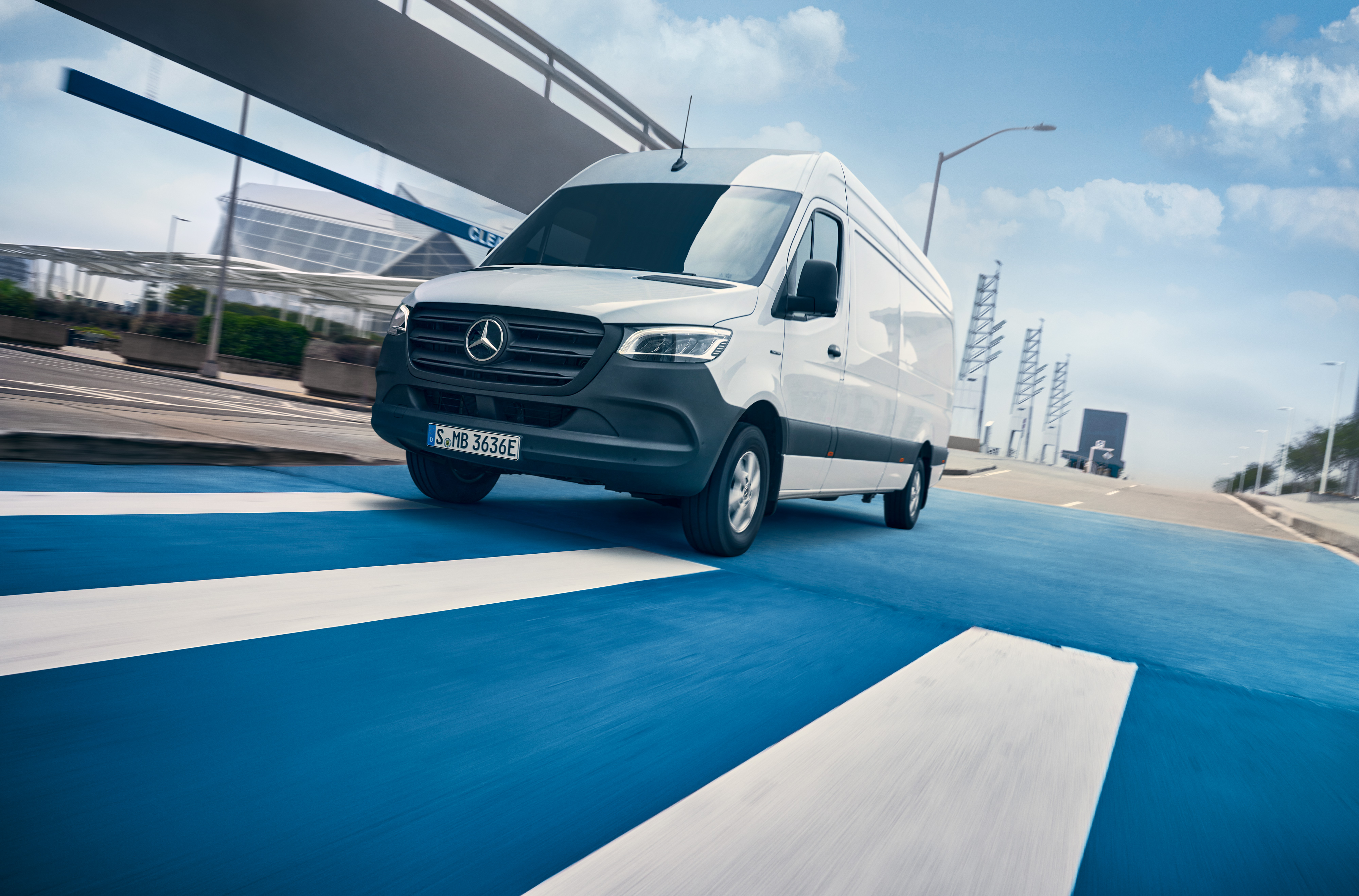 Mercedes-Benz | ServiceCare veículos comerciais ligeiros | Pacote de manutenção Um Mercedes-Benz Sprinter branco circula numa estrada que atravessa uma cidade.