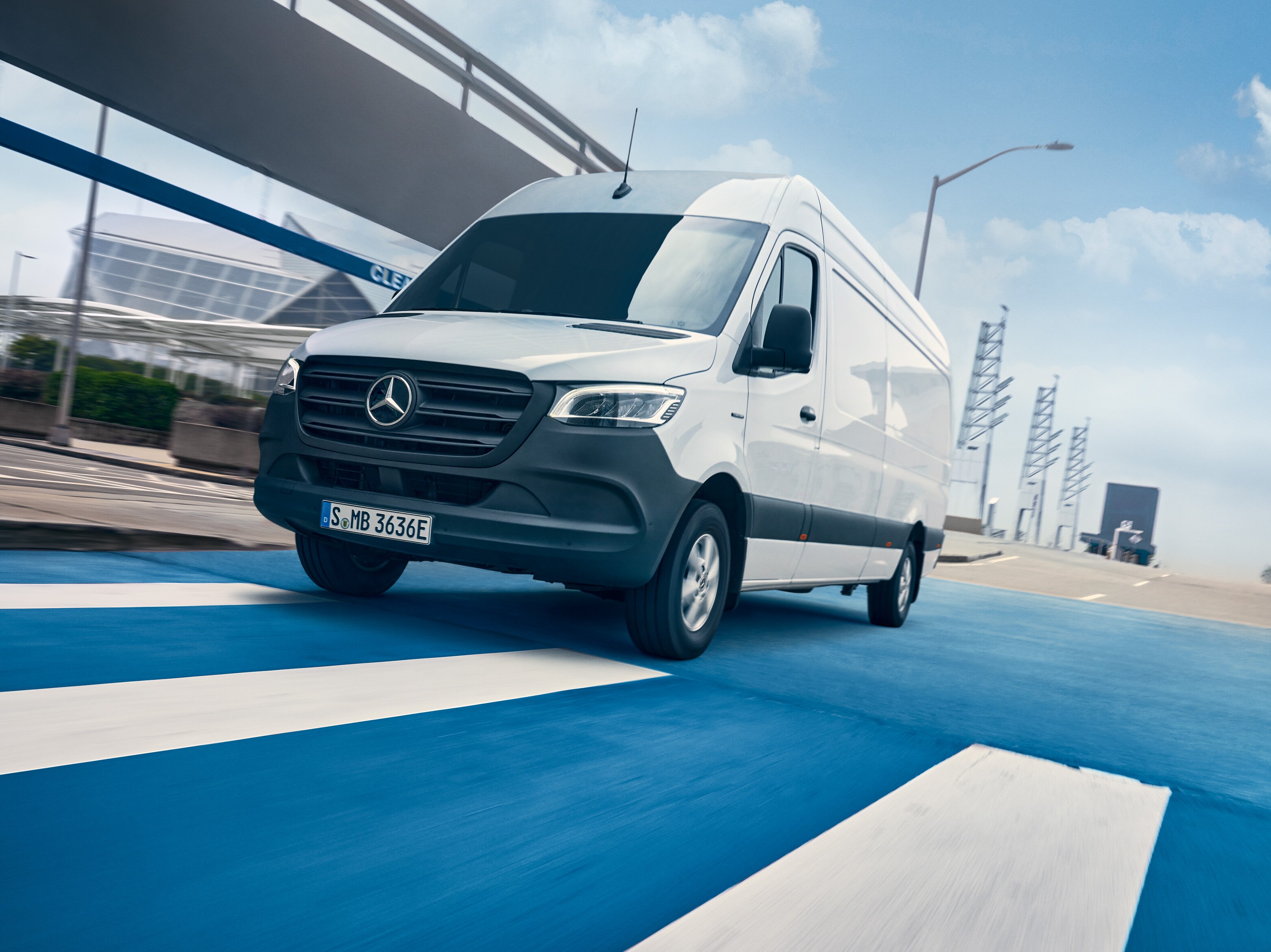 Um Mercedes-Benz Sprinter branco circula numa estrada que atravessa uma cidade.