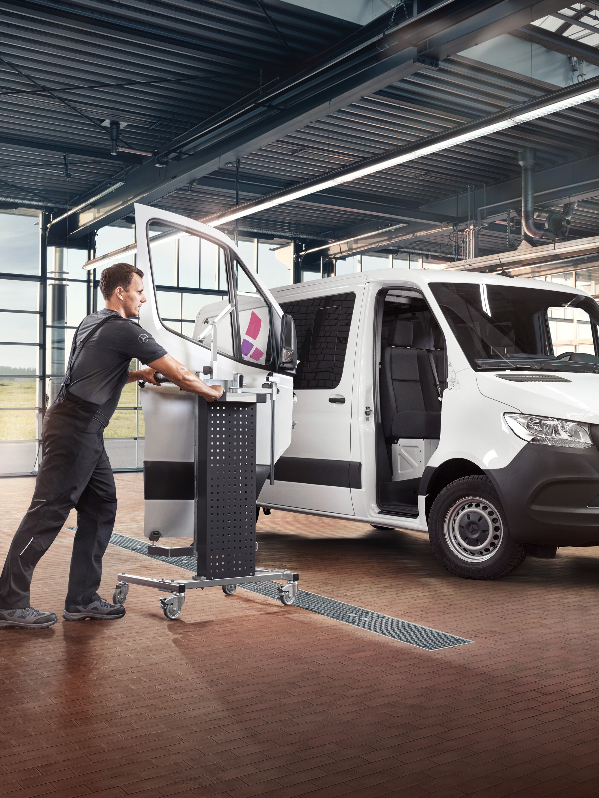 Um técnico faz a manutenção da porta do passageiro de um veículo comercial ligeiro Mercedes-Benz Sprinter branco.