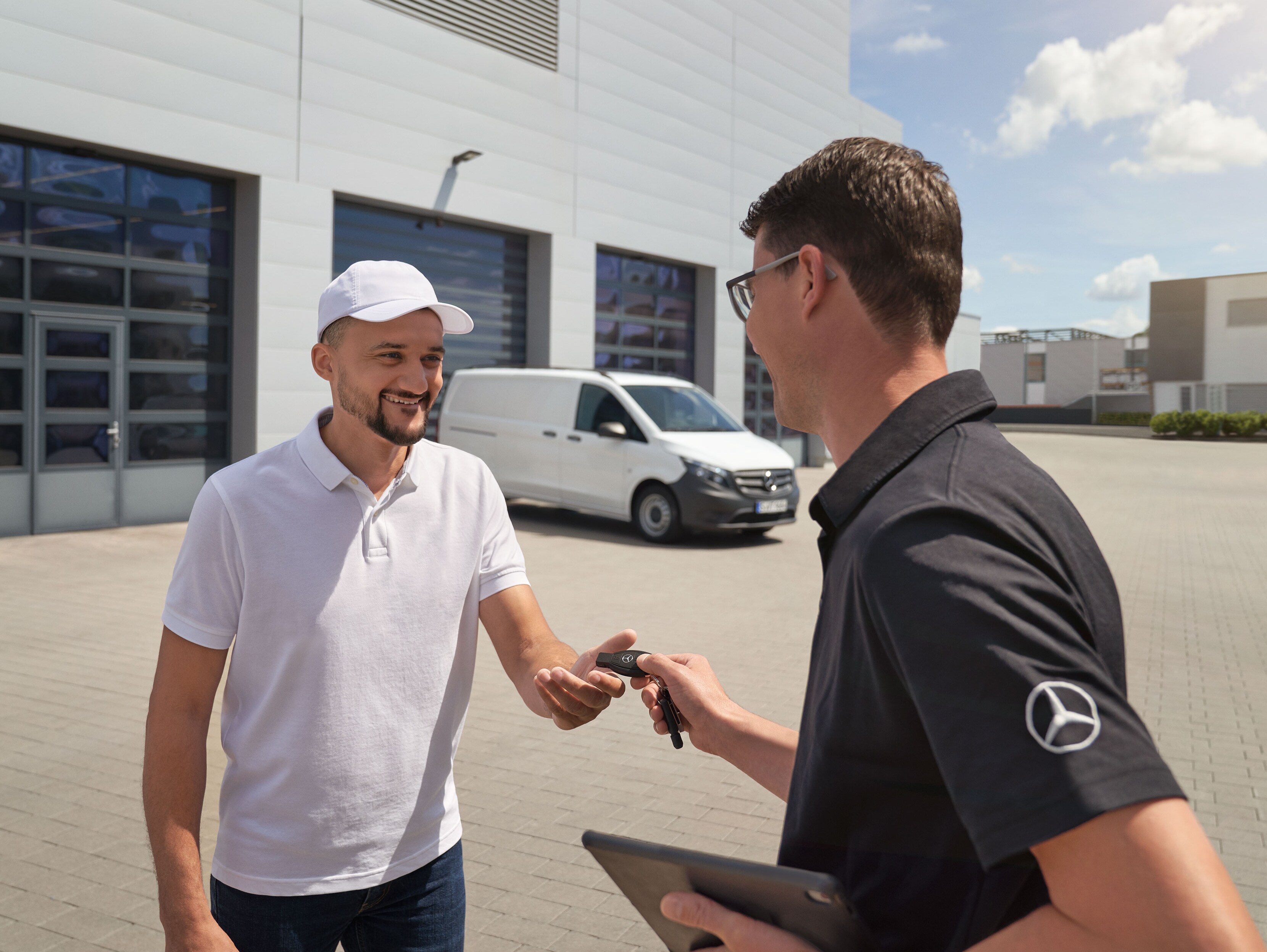Um técnico a entregar o comando a um cliente com um veículo comercial ligeiro Mercedes-Benz Vito branco em segundo plano.