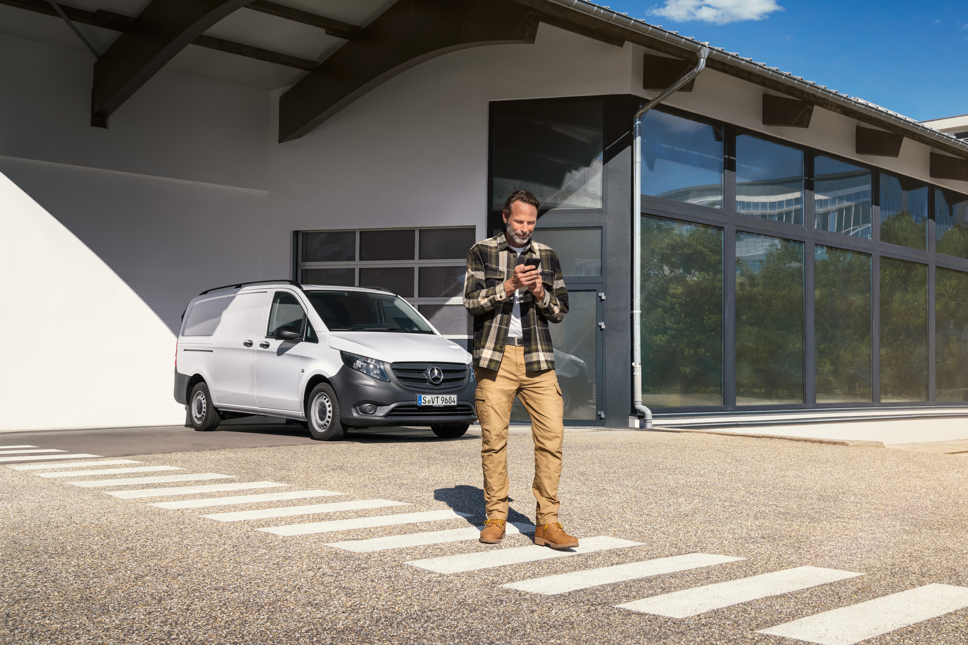 Mercedes-Benz | Serviço para veículos elétricos | Apoio digital Um homem em frente a um veículo comercial ligeiro Mercedes-Benz Vito branca a utilizar o seu smartphone.