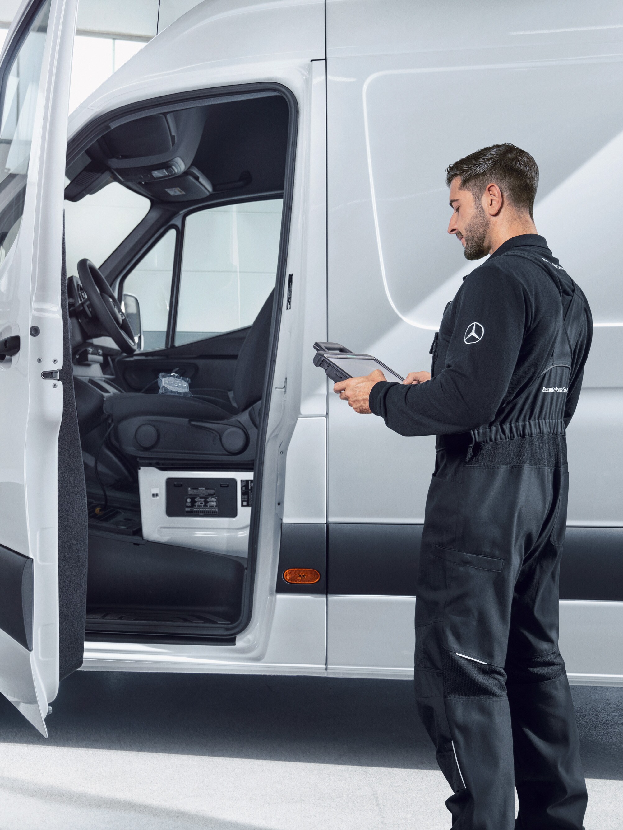 Um técnico verifica um veículo comercial ligeiro Mercedes-Benz Sprinter branco com um tablet.