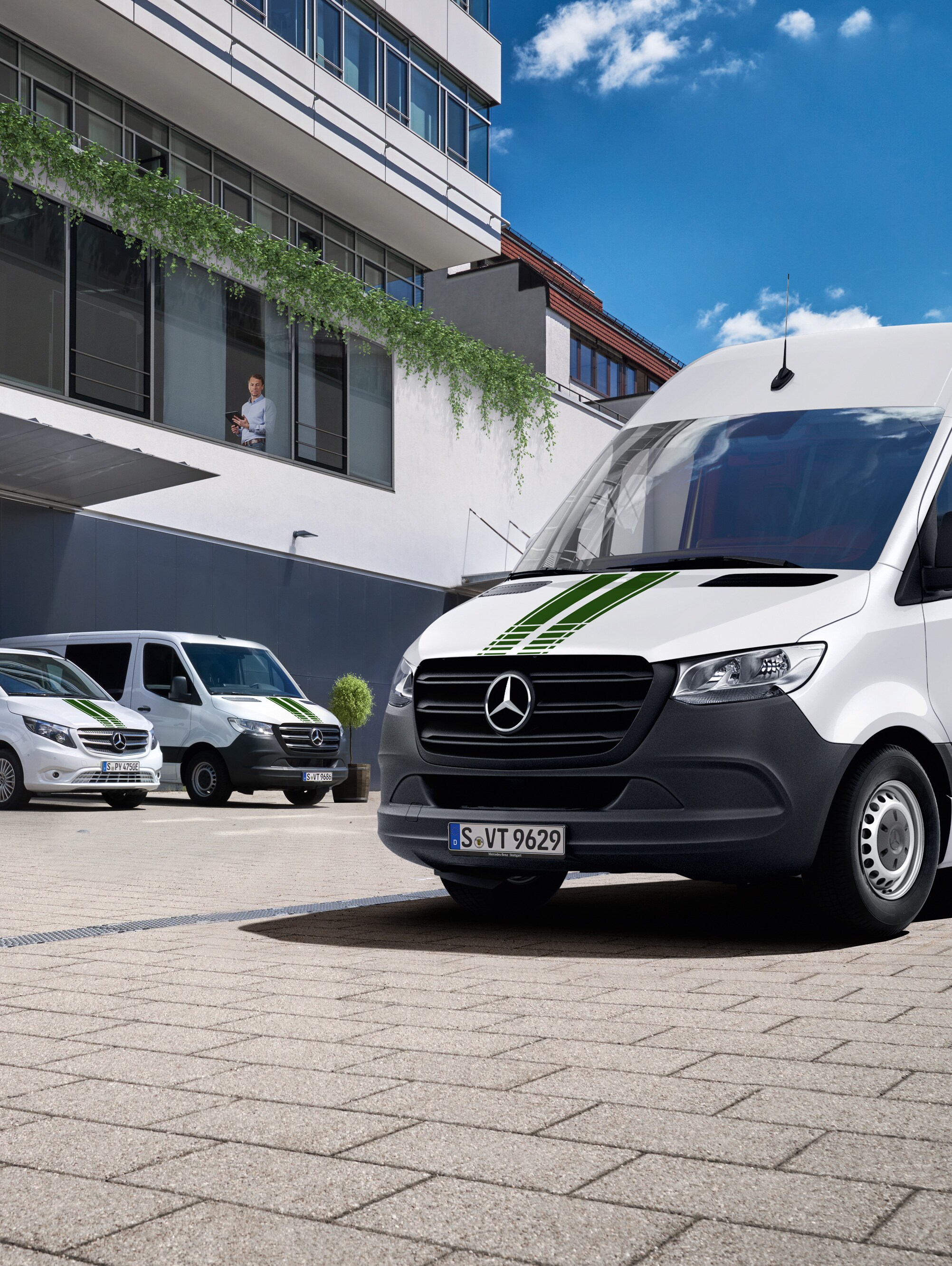 Uma frota de veículos comerciais ligeiros Mercedes-Benz brancos em frente a um edifício de escritórios num dia de sol com céu azul.