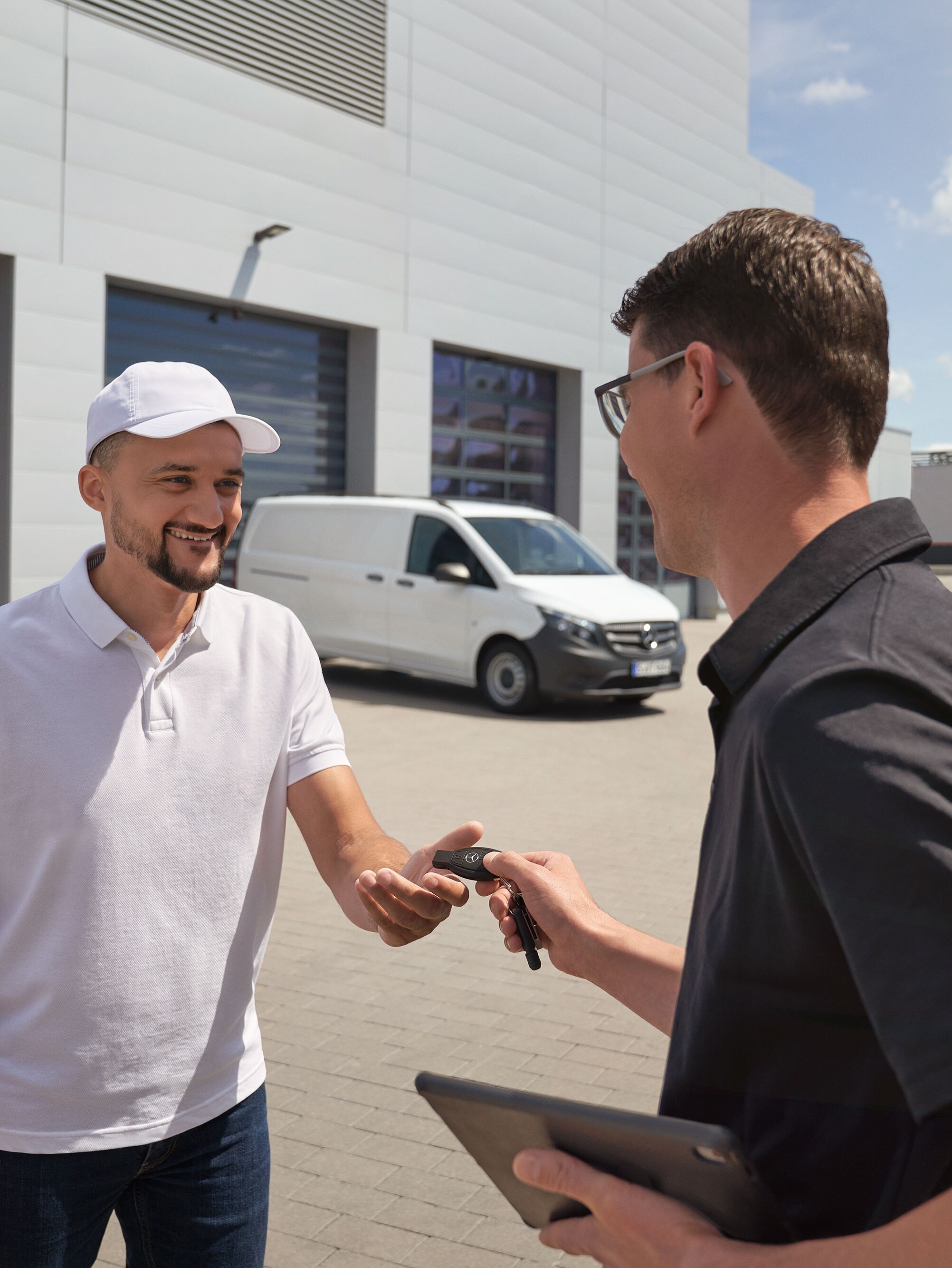 Representante de serviço da Mercedes-Benz a entregar as chaves a um cliente com um veículo comercial ligeiro Mercedes-Benz Vito branco em segundo plano.