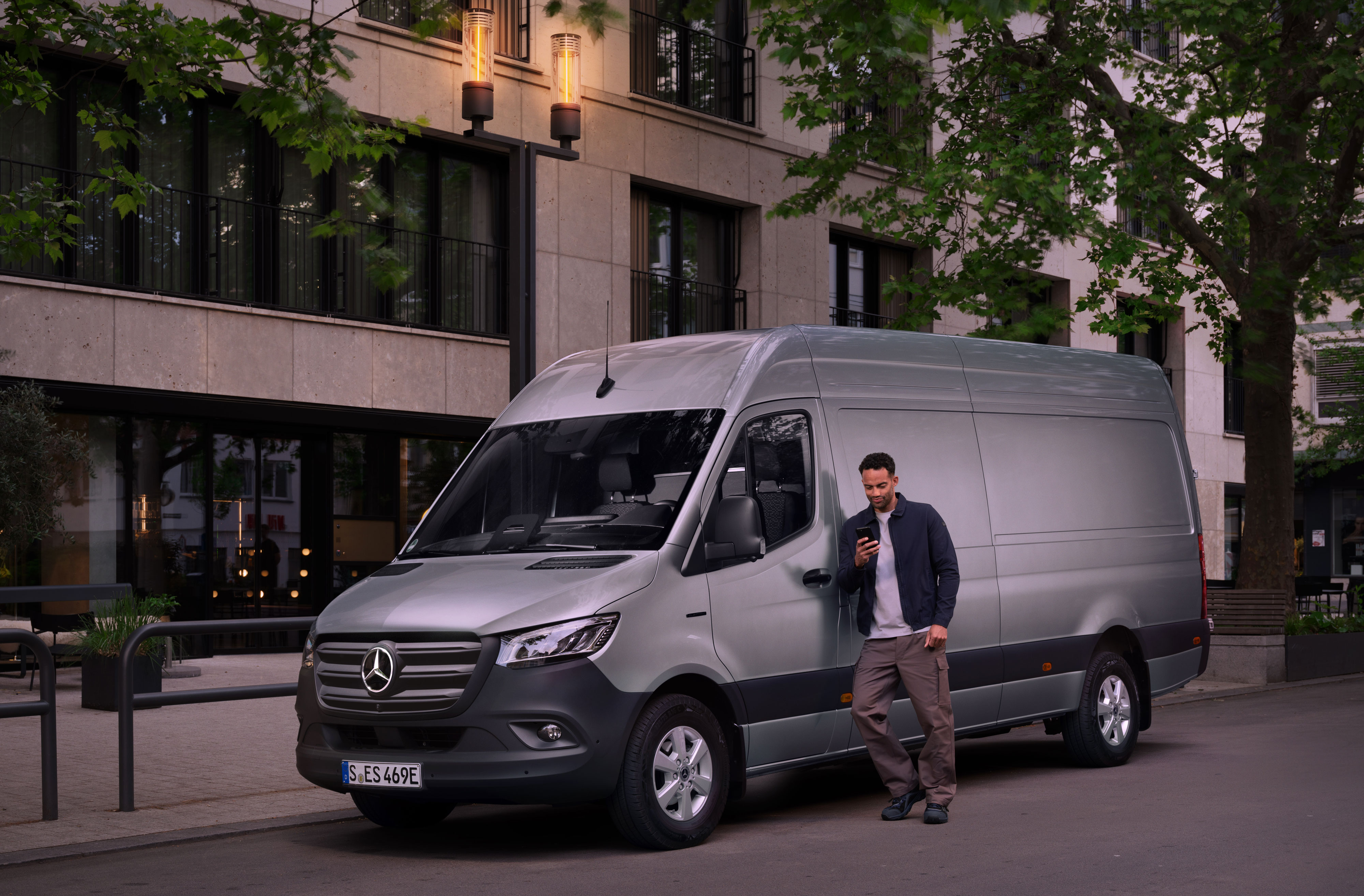 Mercedes-Benz | Reparação | Relatório de danos digital Homem encostado a um Mercedes-Benz Sprinter prateado e a preencher um relatório de danos no seu telemóvel.