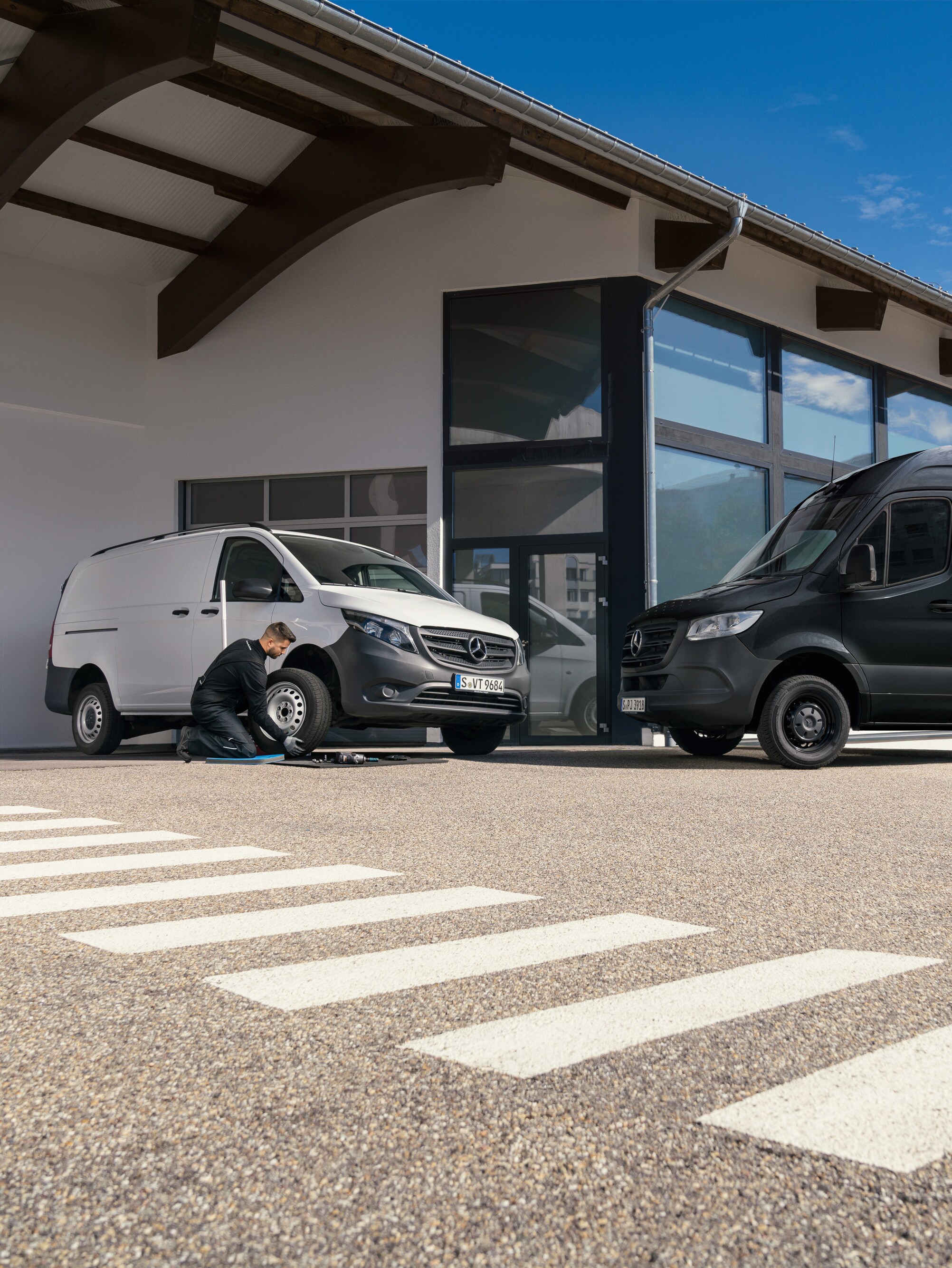 Um técnico muda um pneu de um veículo comercial ligeiro Mercedes-Benz Vito branco em frente a uma sala de exposições.