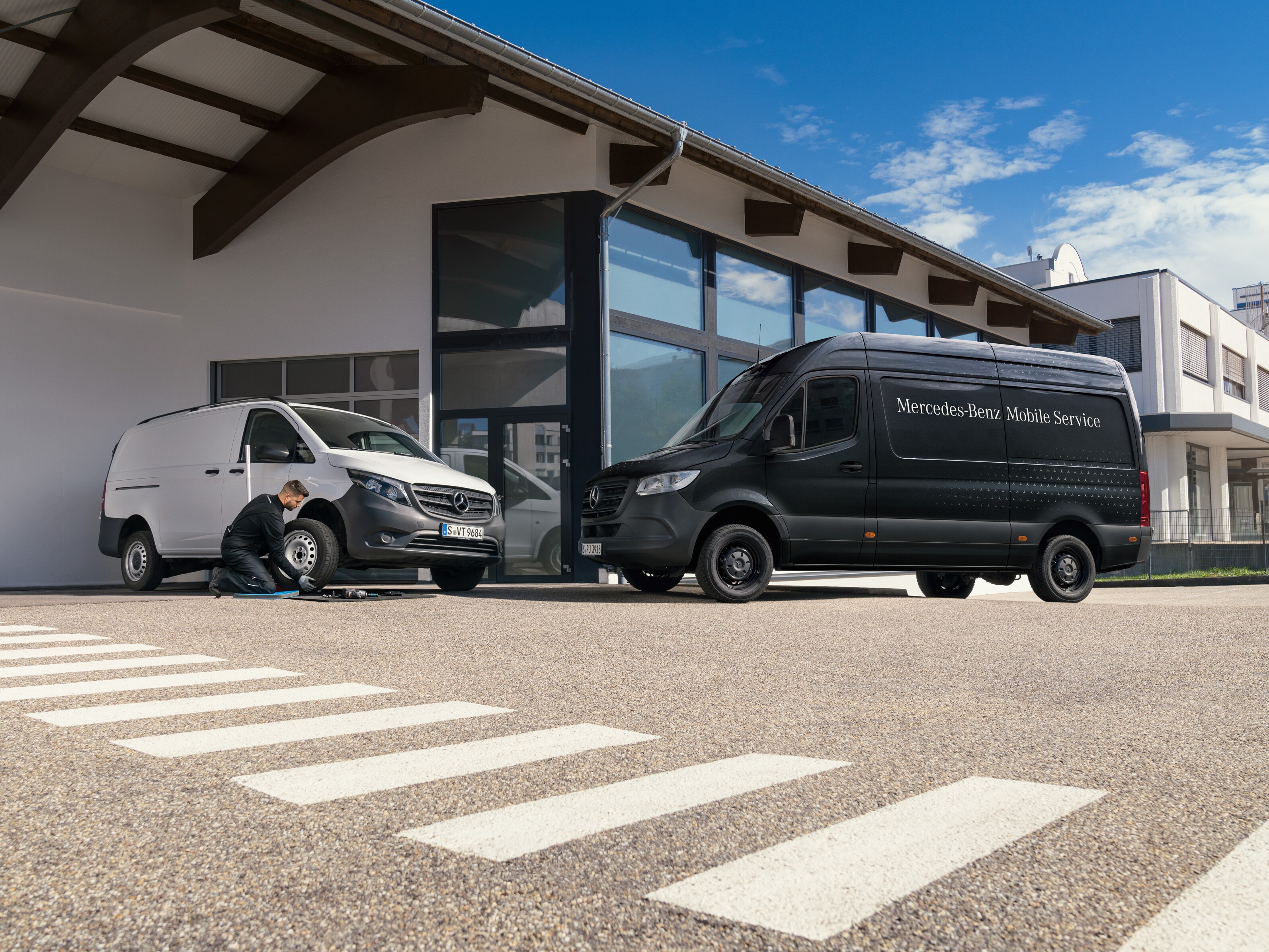 Um técnico muda um pneu de um veículo comercial ligeiro Mercedes-Benz Vito branco em frente a uma sala de exposições.