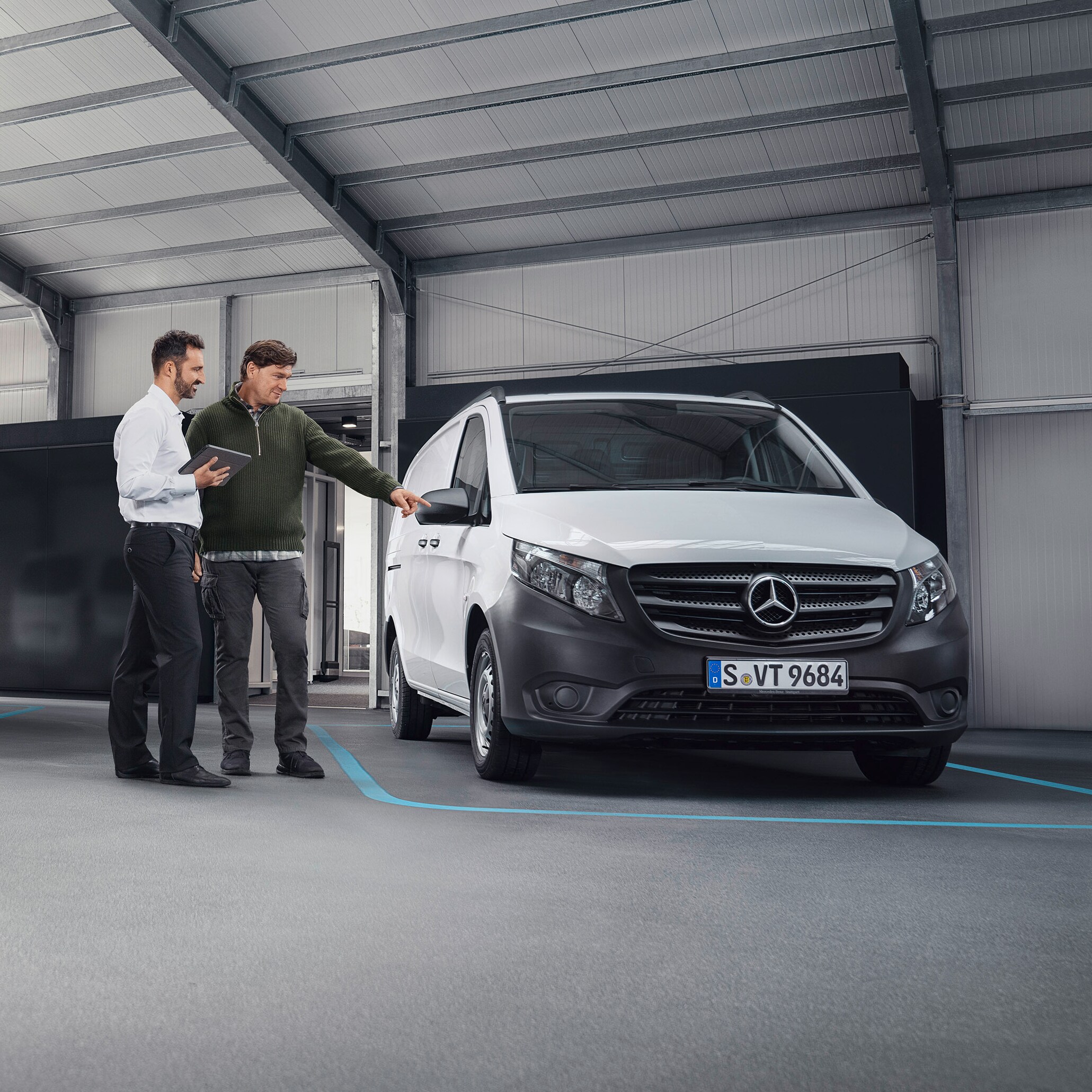 Agente do atendimento ao cliente da Mercedes-Benz com cliente nas instalações de uma oficina autorizada em frente a um veículo comercial ligeiro.
