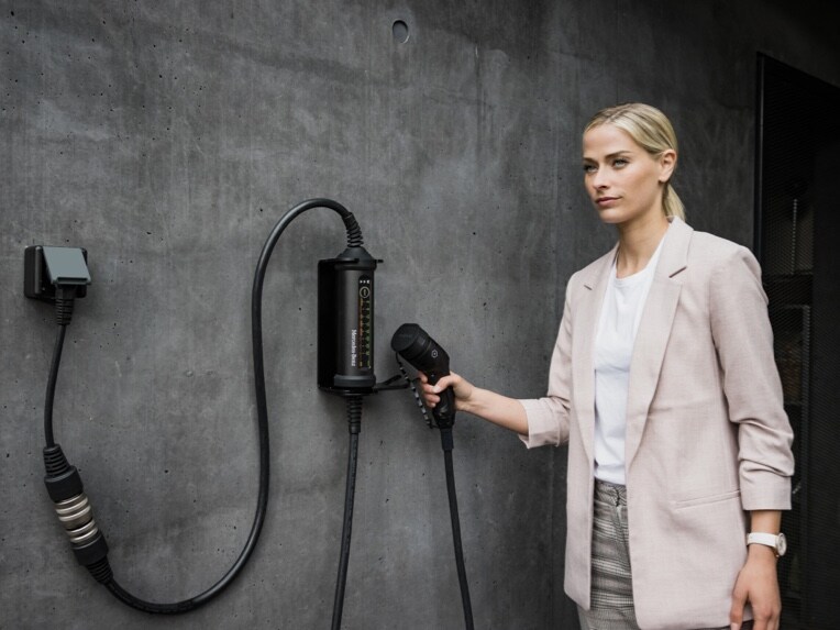 Uma pessoa a utilizar o sistema de carregamento flexível da Mercedes-Benz com cabo e respetivo adaptador.
