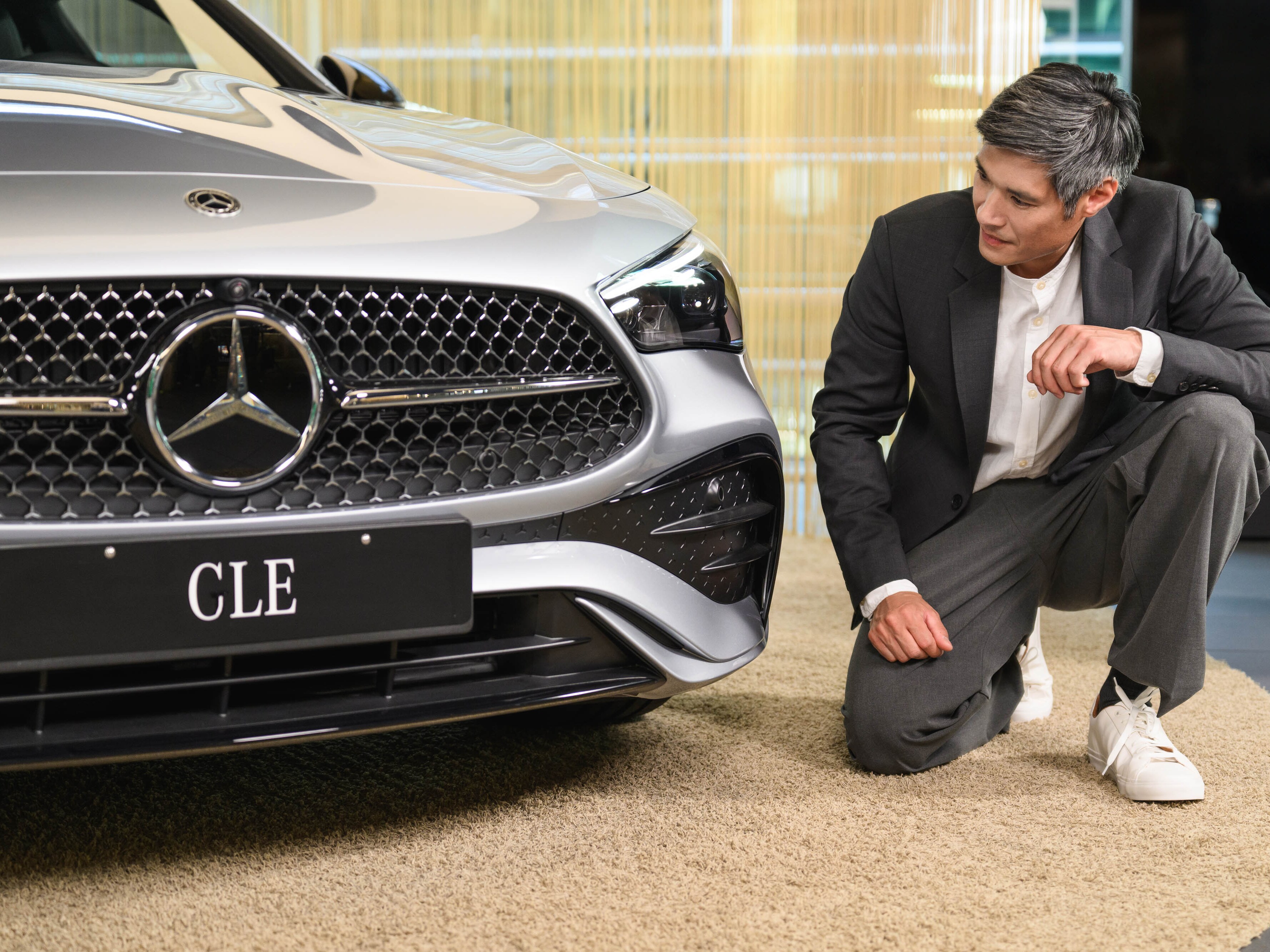 Uma pessoa com um joelho no chão a olhar para a grelha de um Mercedes-Benz.