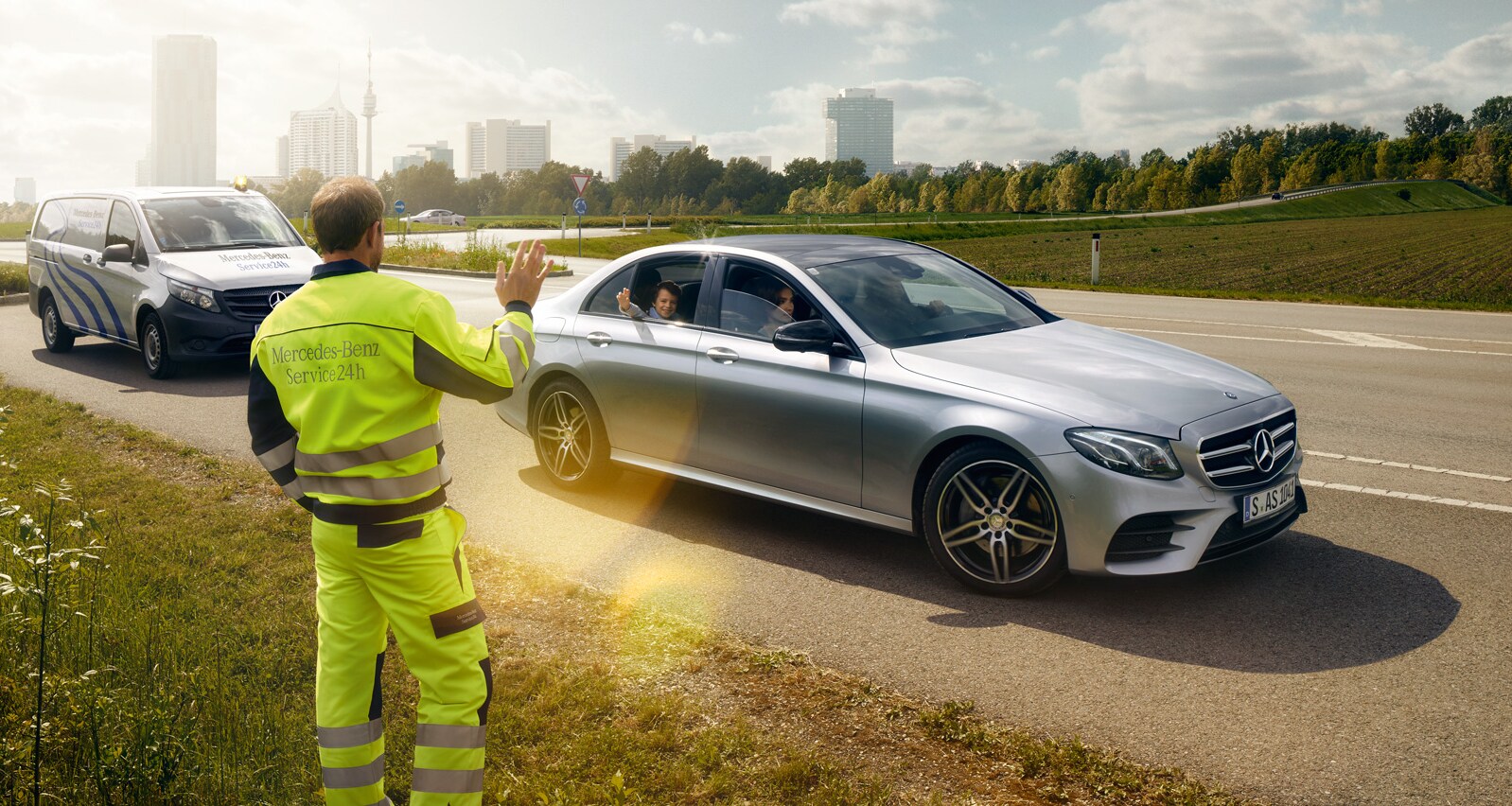 Através do para-brisas de um Mercedes, vemos um técnico de serviço parado ao lado da condutora, à frente do veículo, apontando de forma explicativa.
