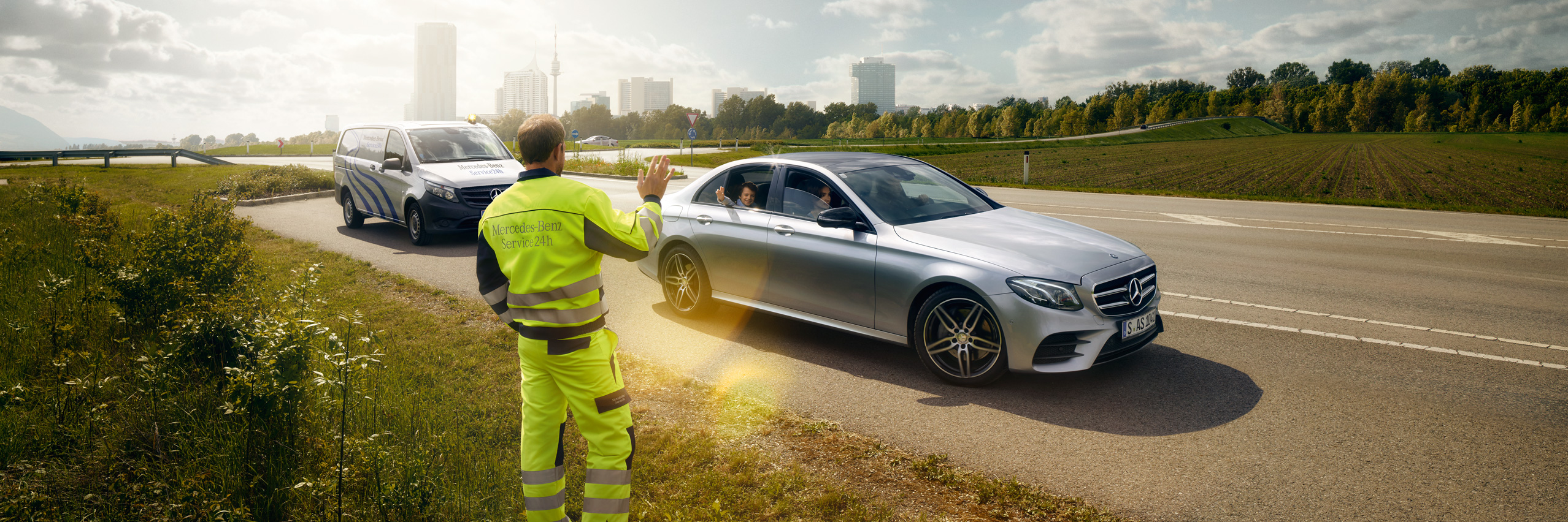 Assistência em caso de avaria ou danos | Mercedes-Benz Através do para-brisas de um Mercedes, vemos um técnico de serviço parado ao lado da condutora, à frente do veículo, apontando de forma explicativa.